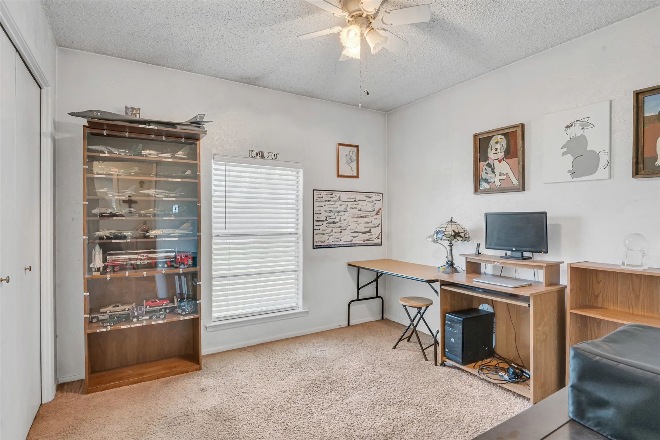 Carpeted interior space featuring a ceiling fan, a window with horizontal blinds, and a built-in display cabinet