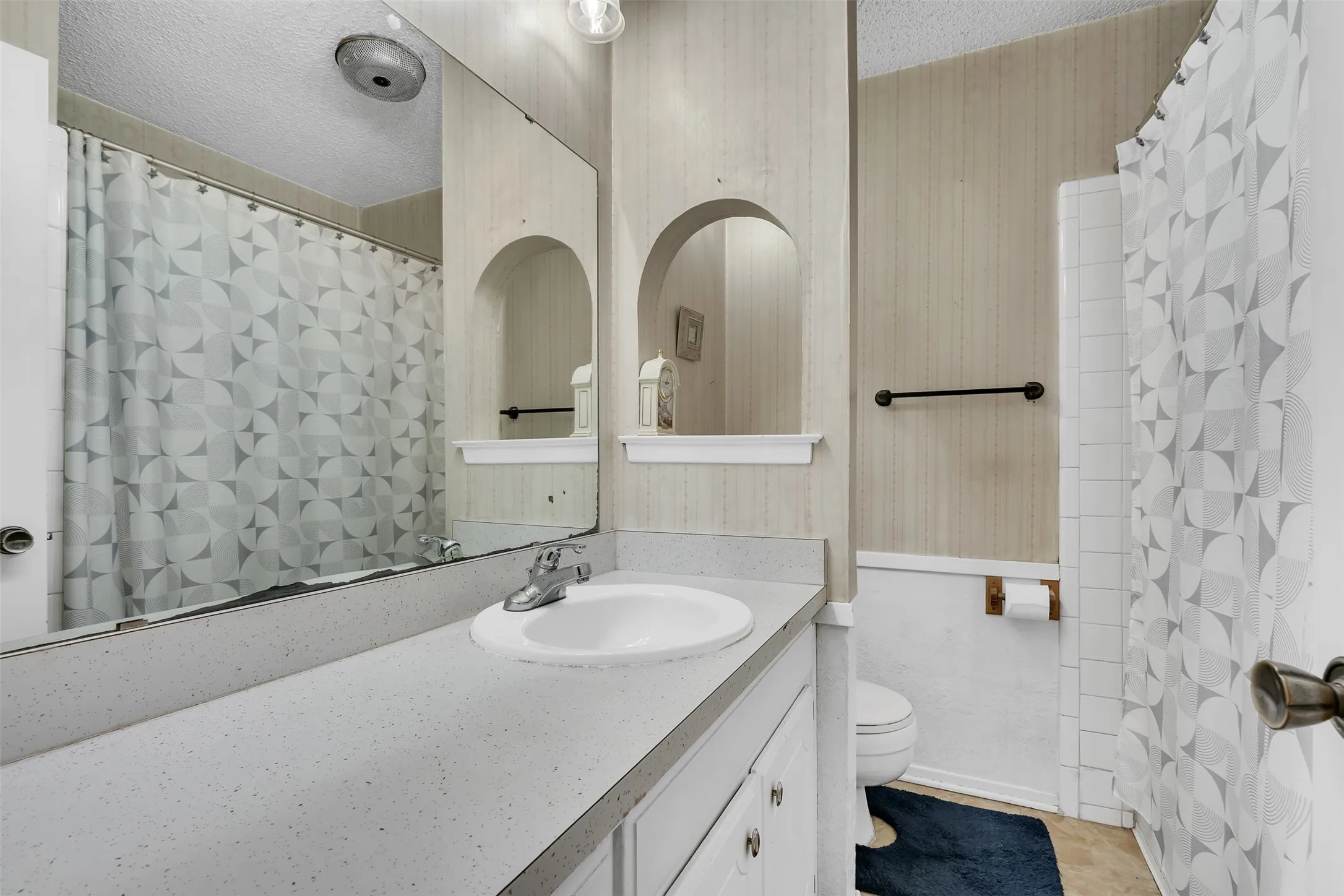 Bathroom featuring a single vanity with an integrated sink and chrome faucet, a wall-mounted mirror, and a shower-tub combination with white tile surround