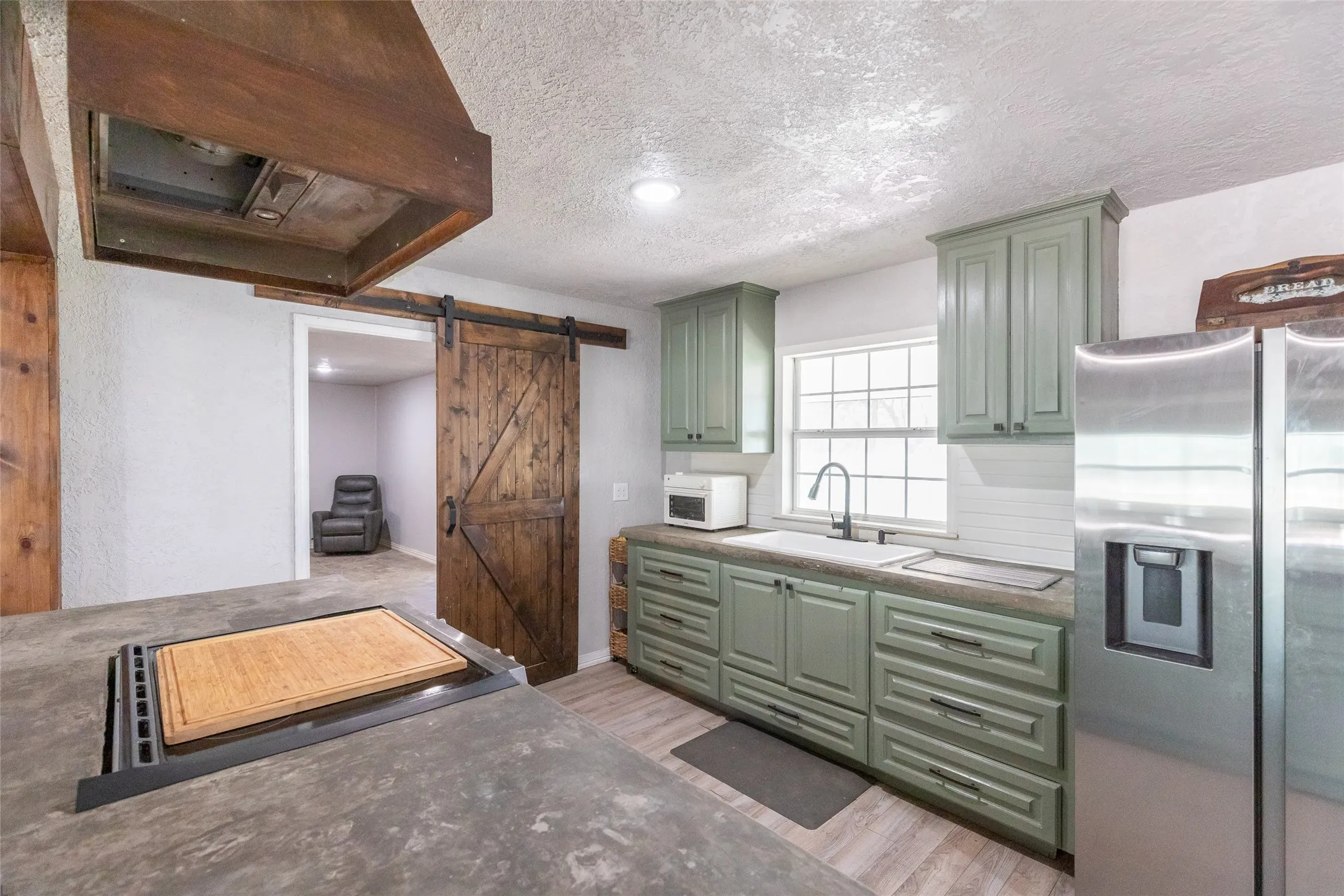 Kitchen featuring sage green cabinetry, a white subway tile backsplash, a built-in stainless steel refrigerator, and a dark wood barn door