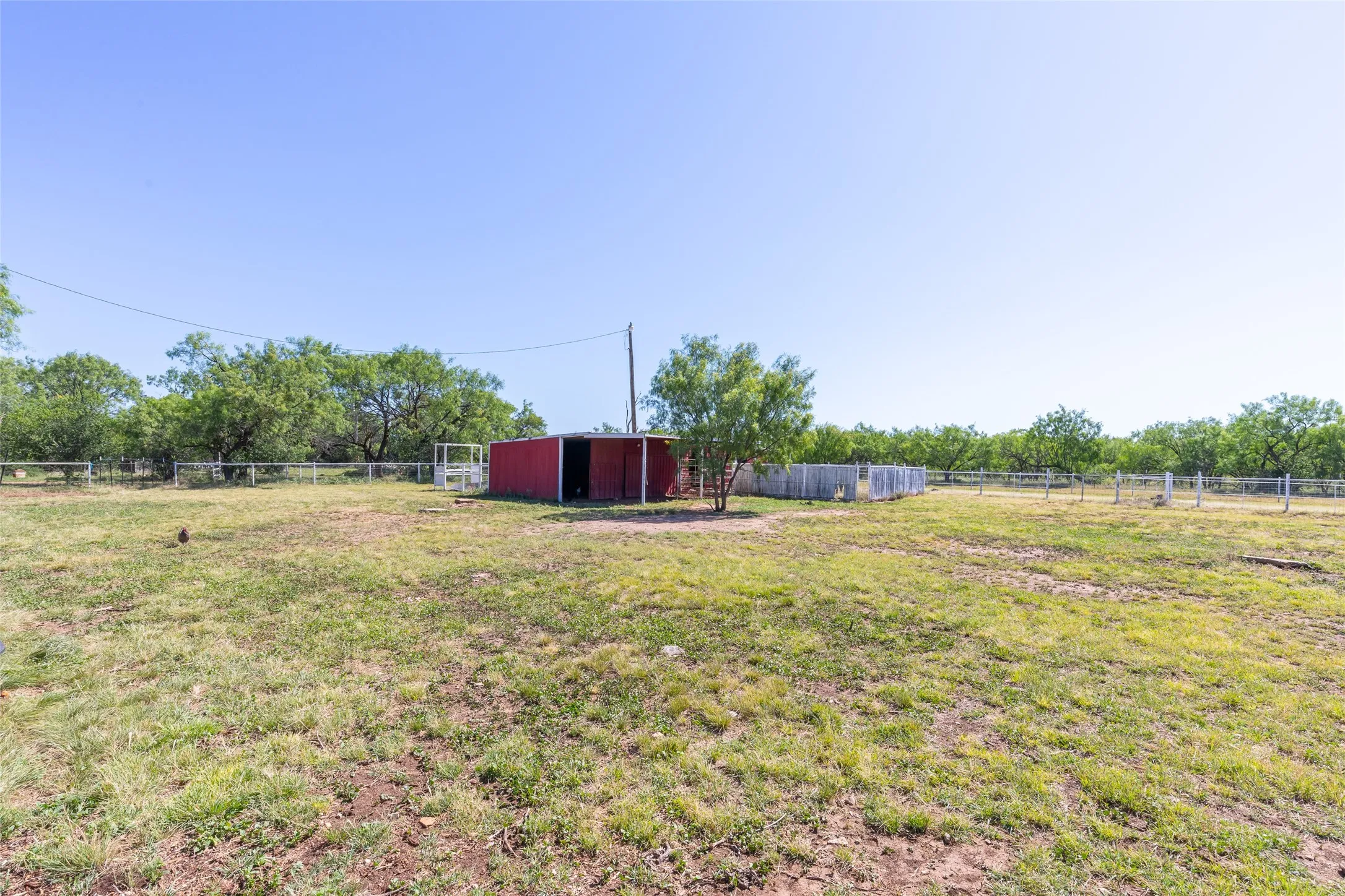 Expansive outdoor property with a red metal outbuilding, wire fencing, and mature trees