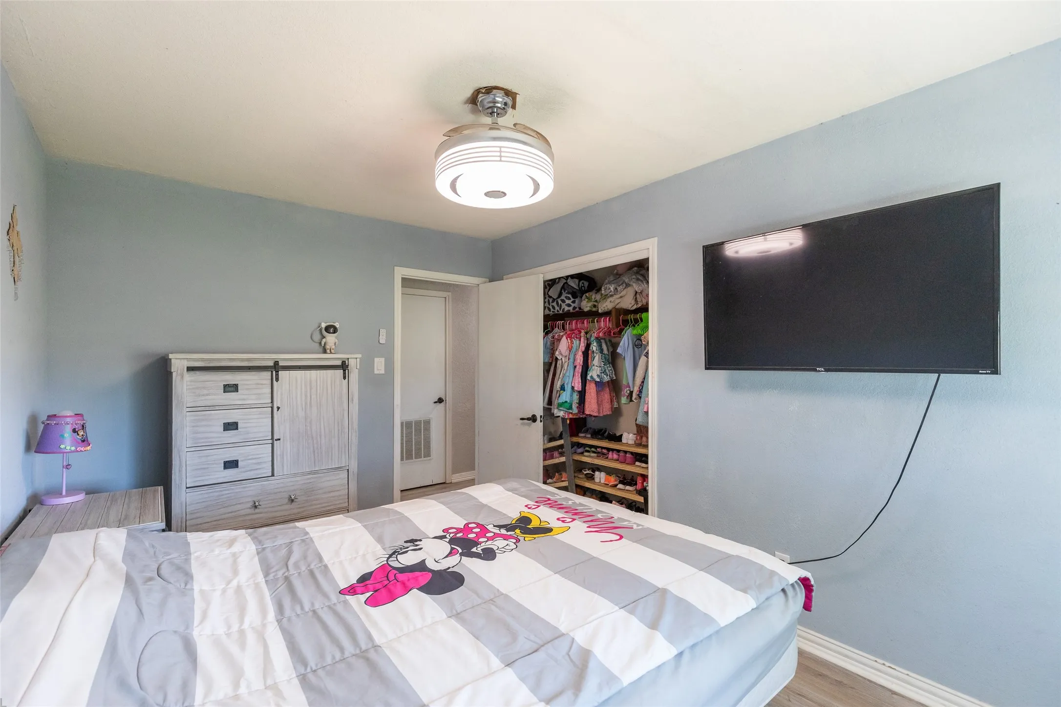 Bedroom featuring light blue walls, wood-finish flooring, and a ceiling-mounted light fixture