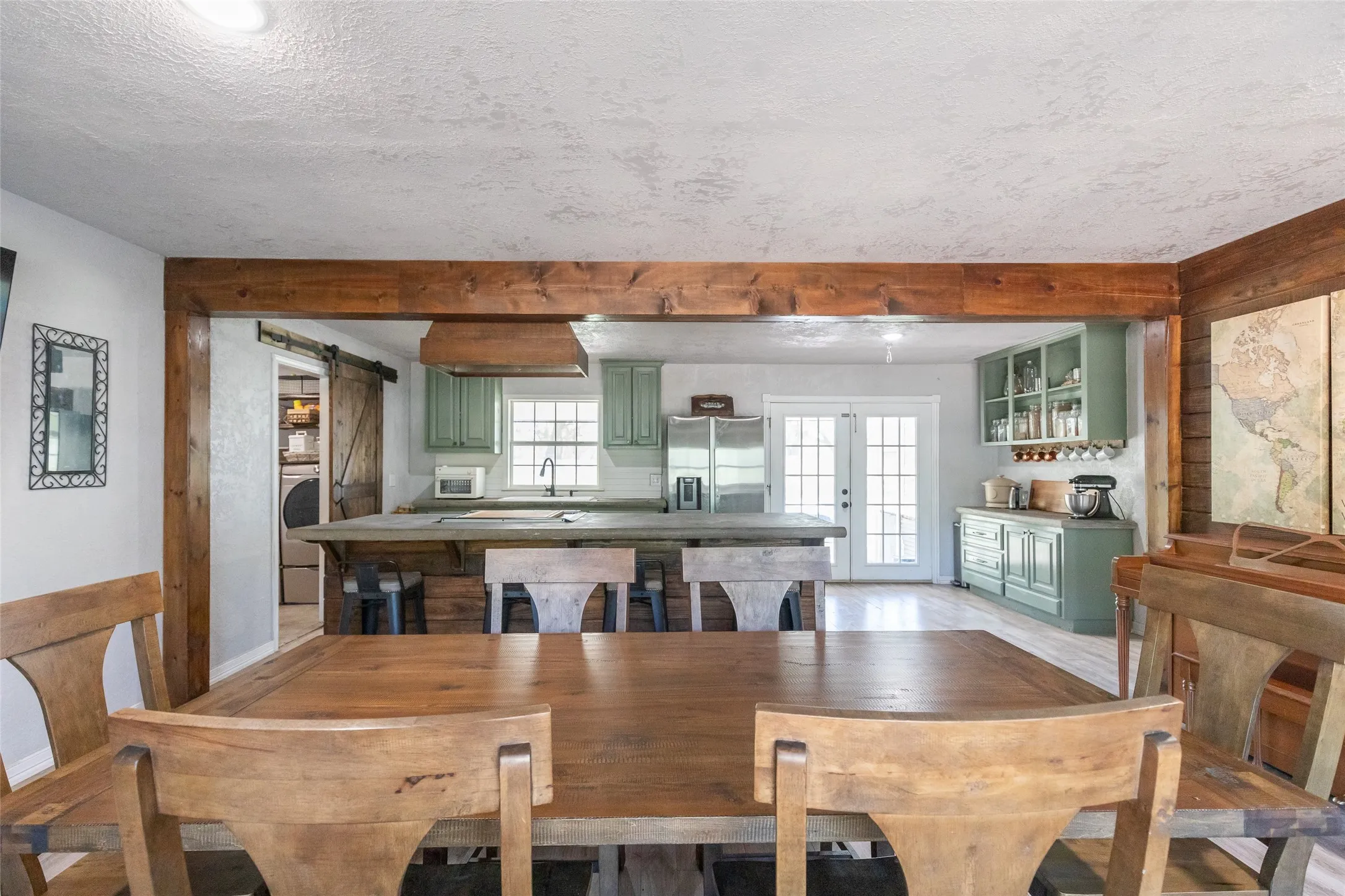Open-concept dining and kitchen area featuring a wood-finish dining table, exposed wood-finish beams, and light green cabinetry