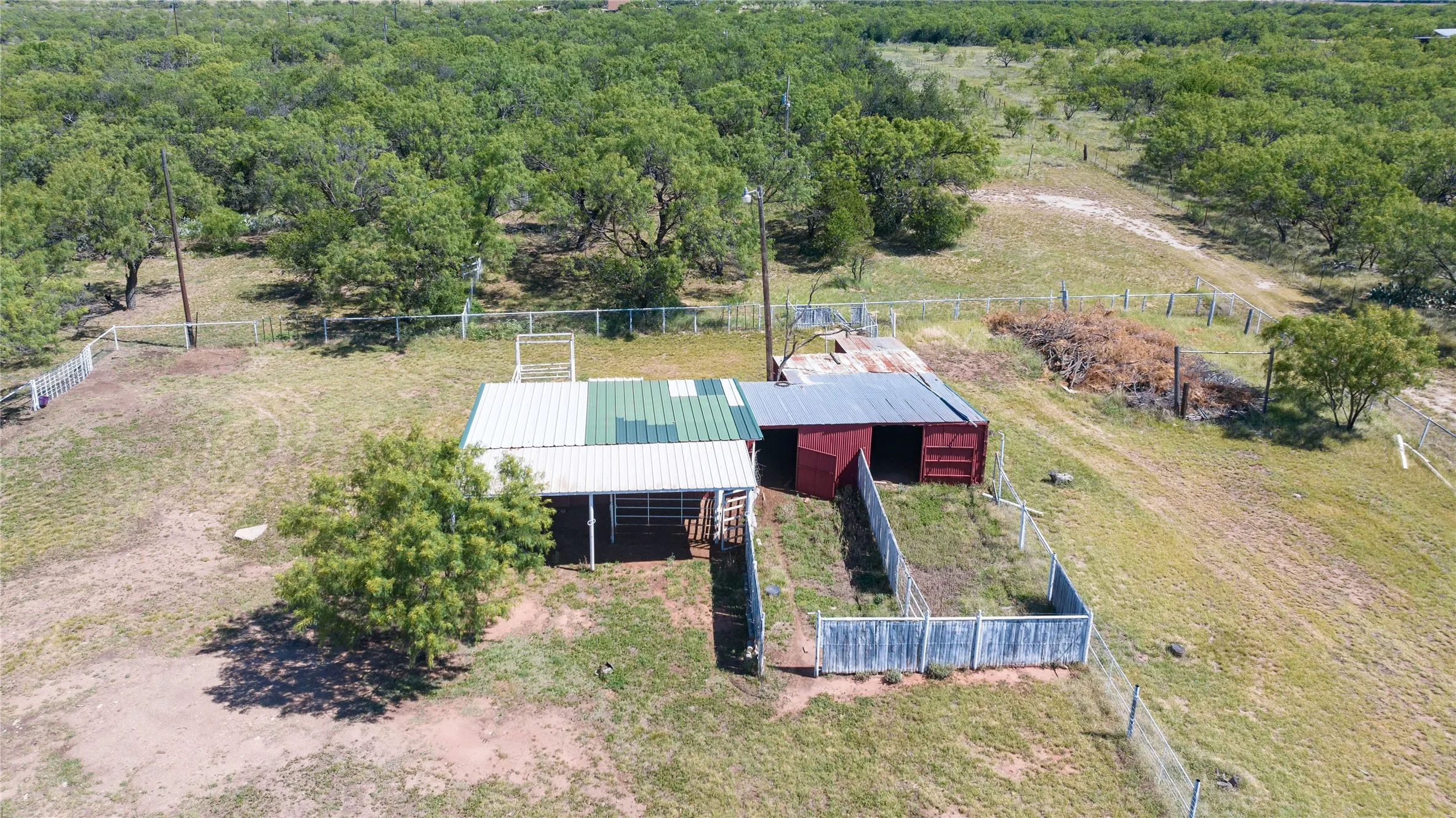 Rustic outbuilding featuring an open-sided structure with a metal roof and an enclosed red structure with a corrugated metal roof