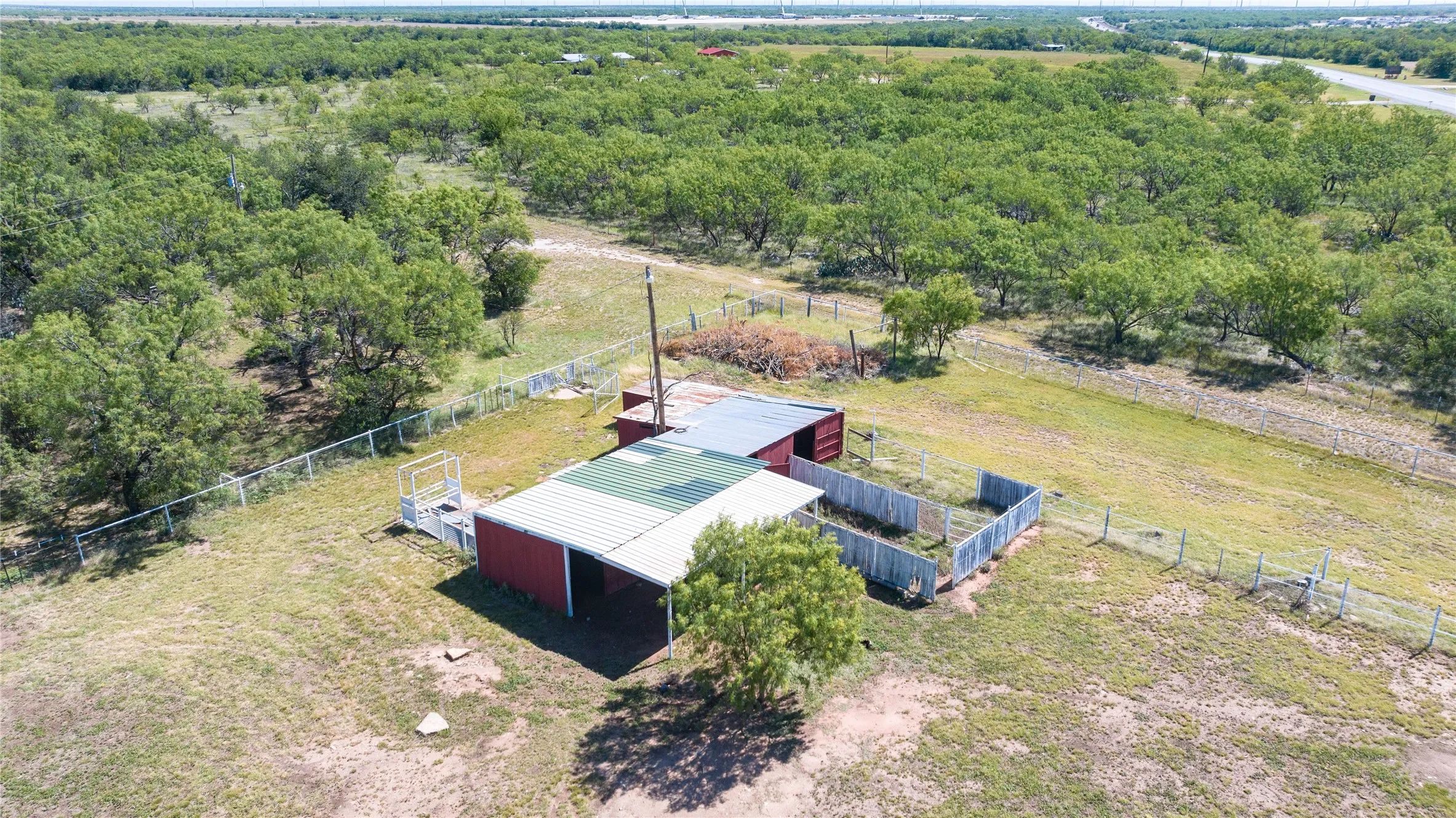 Red-sided barn structure with an extended corrugated metal roof and fenced enclosures