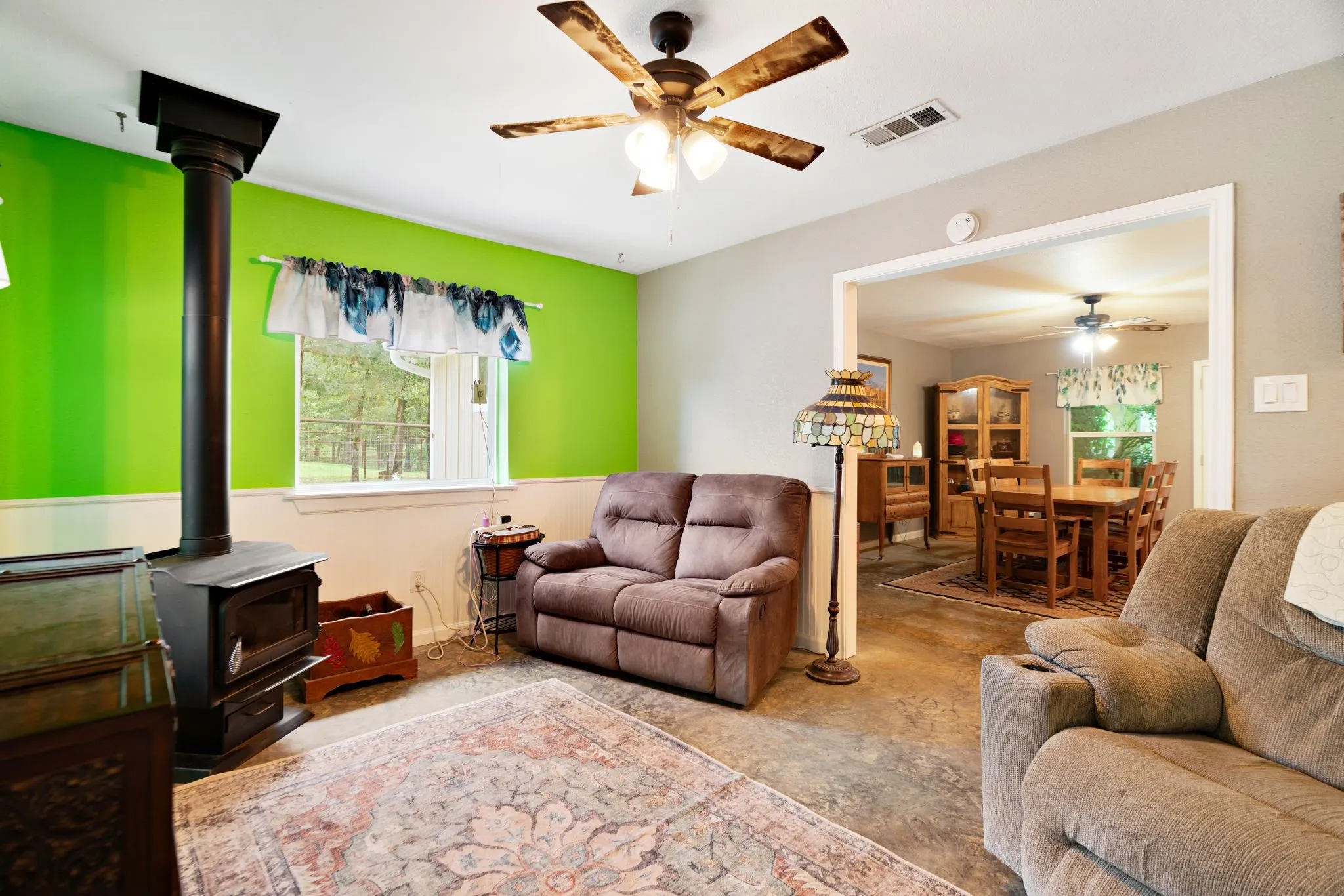Living area featuring a freestanding wood-burning stove, ceiling fan with light fixture, and a window with exterior views