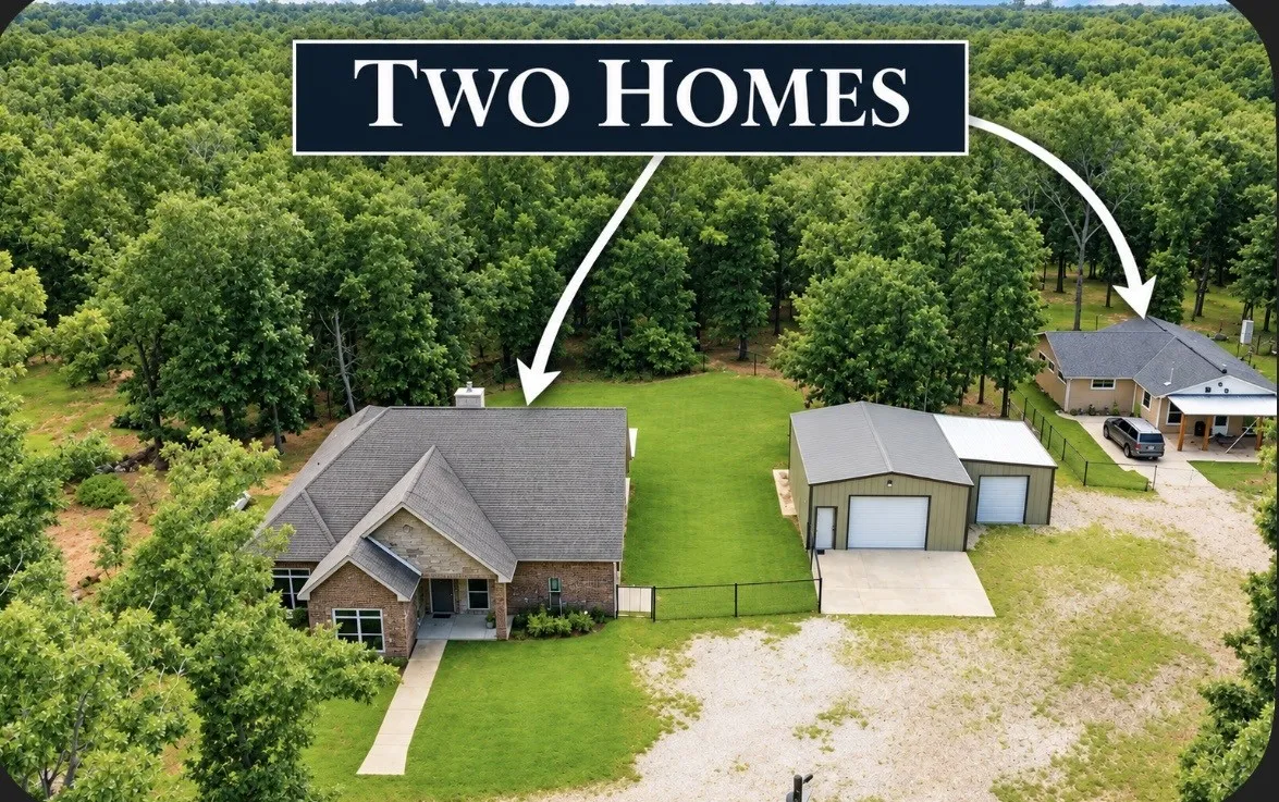 Two distinct homes on a wooded lot, featuring a primary residence with brick and stone accents, a secondary residence, and a multi-bay detached garage/workshop