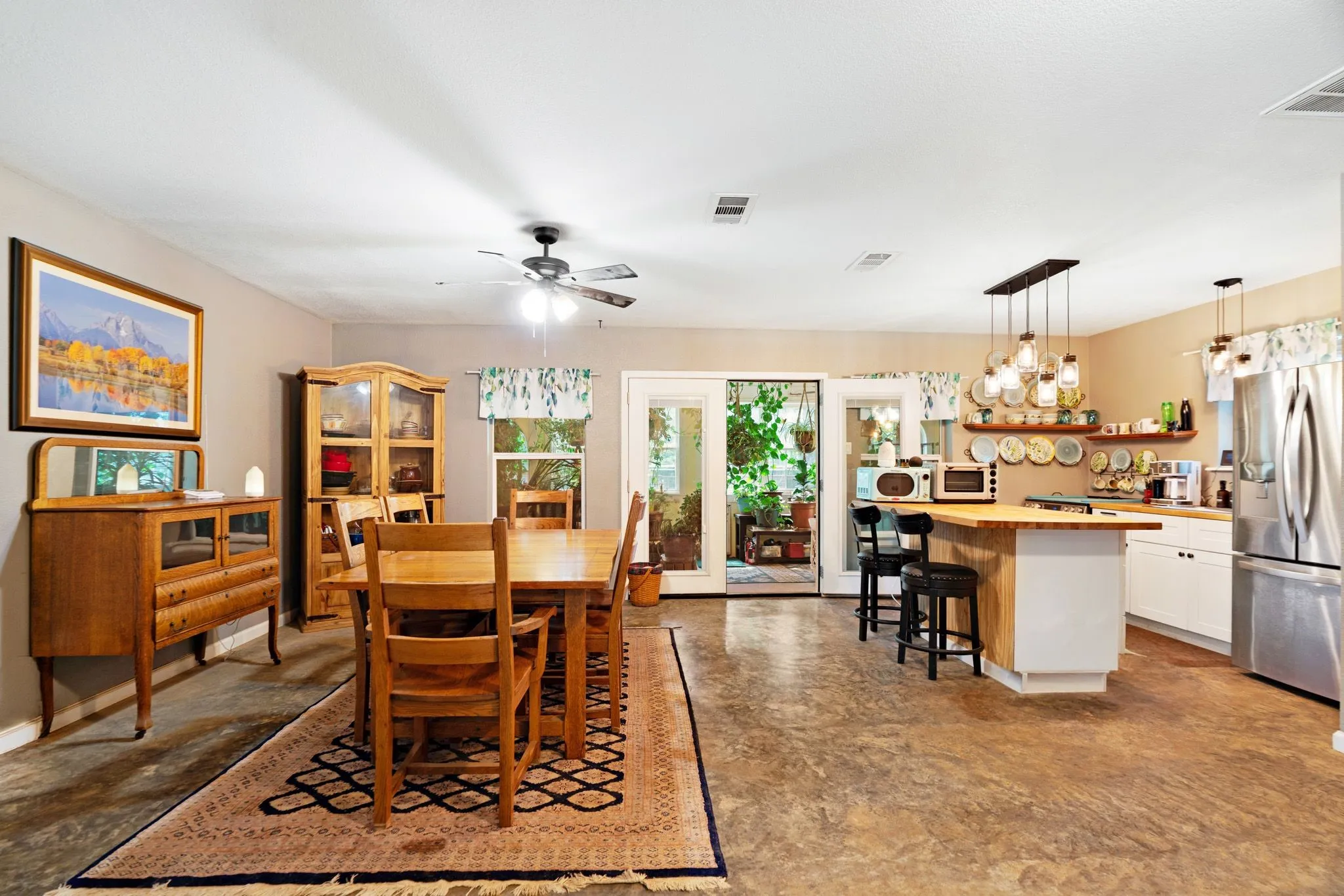 Spacious eat-in kitchen and dining area featuring a kitchen island with wood-finish countertop, white cabinetry, stainless steel refrigerator, and glass-paneled patio doors