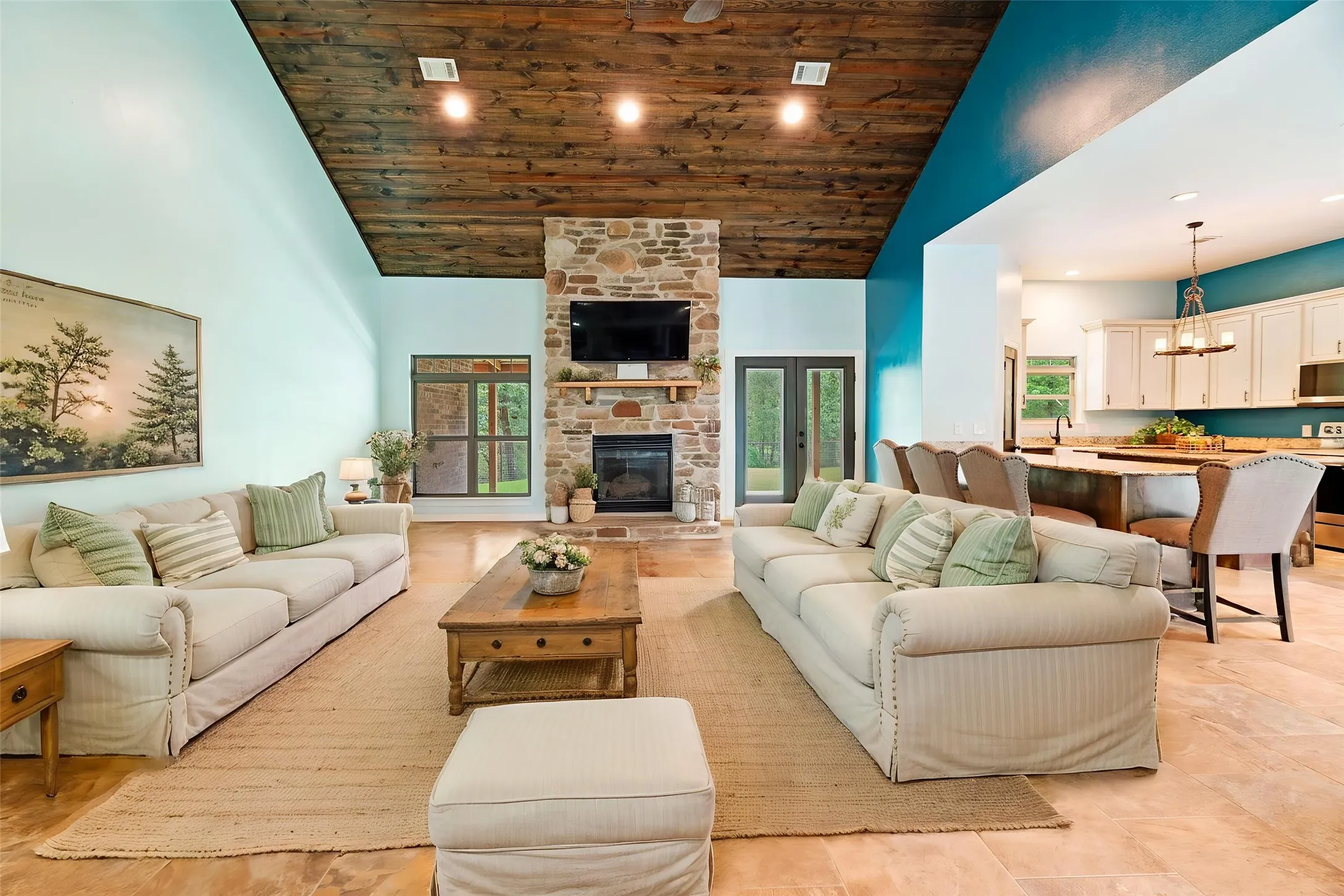 Spacious living area featuring a vaulted wood-finish ceiling, stone fireplace with hearth, and tiled flooring
