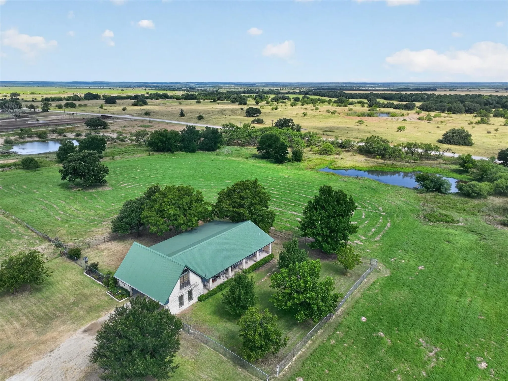 Stone exterior residence with a green metal roof, surrounded by expansive green fields and mature trees