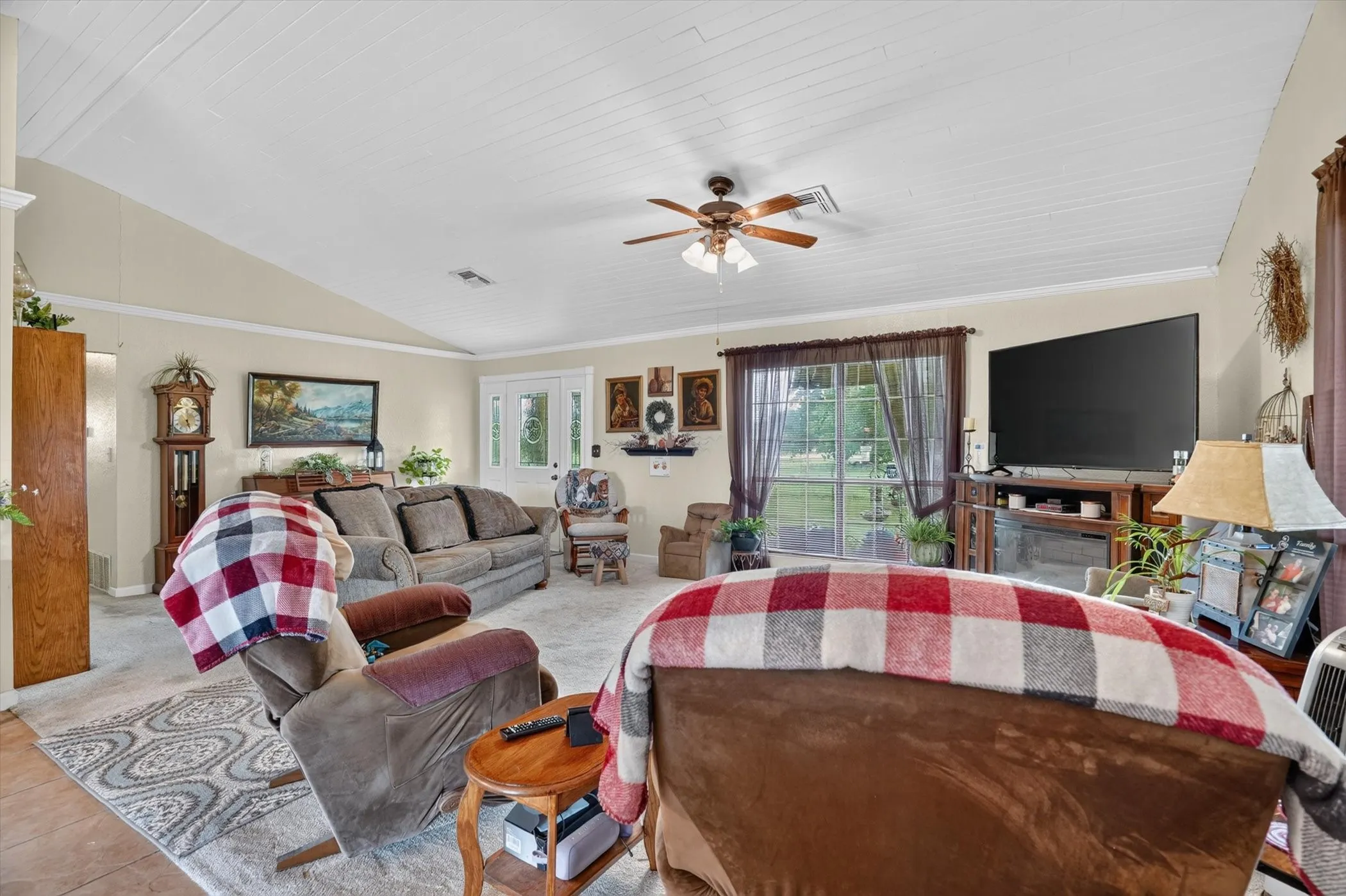 Spacious living area featuring a vaulted ceiling with white planking, a ceiling fan with integrated lighting, and crown molding
