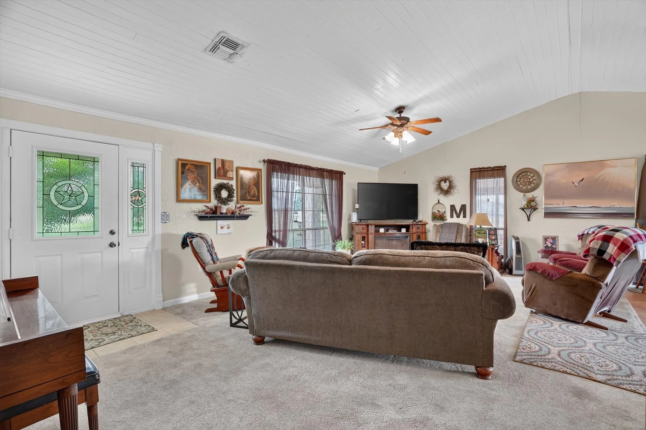 Living area featuring vaulted ceilings with wood-finish paneling, an entryway with decorative glass sidelights, and a ceiling fan