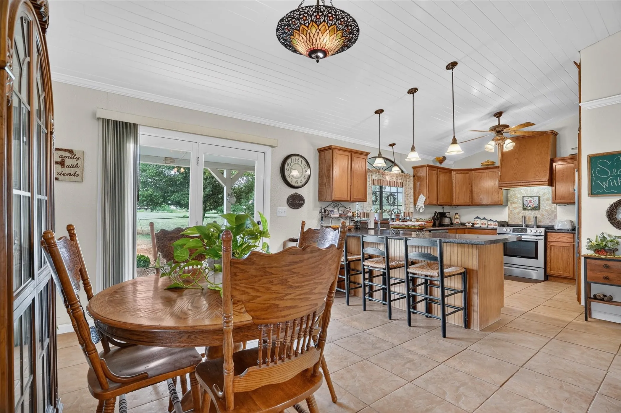 Kitchen and dining area featuring a beadboard ceiling, tile flooring, wood cabinetry, a center island with pendant lighting, and stainless steel appliances