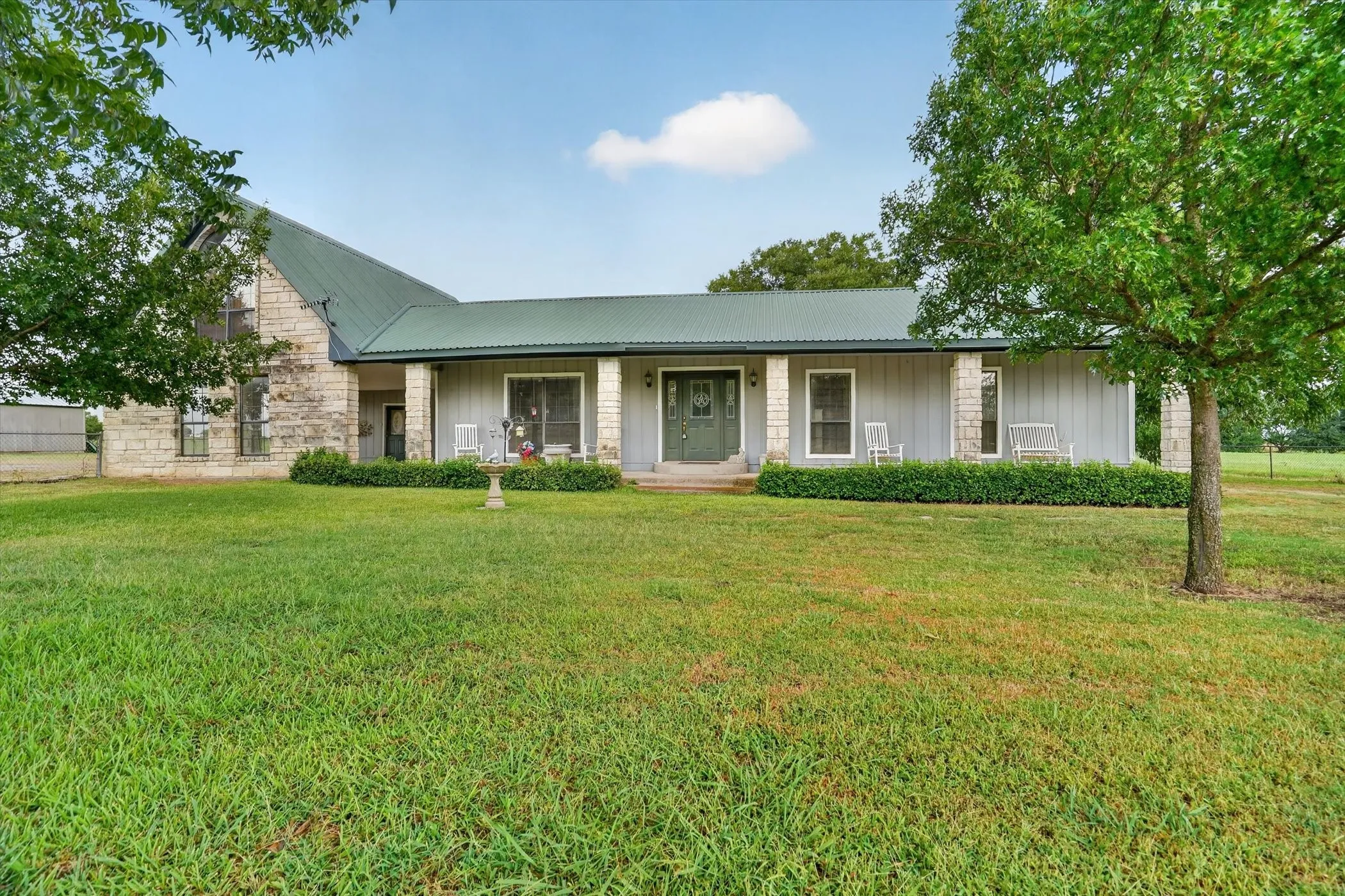 Exterior featuring a green metal roof, stone and siding facade, and a covered front porch with columns