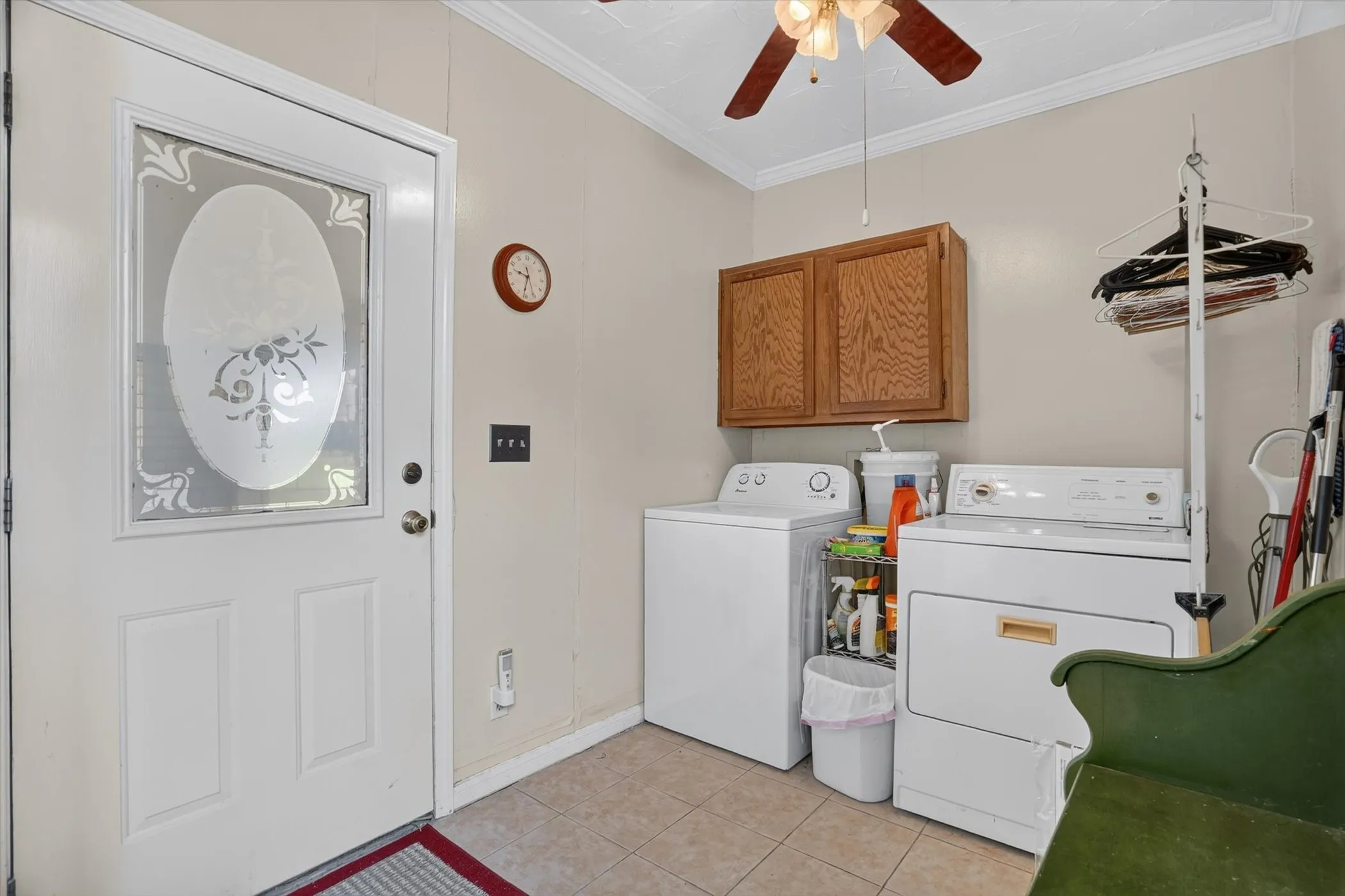 Dedicated laundry area featuring tile flooring, wood-finish upper cabinetry, and a ceiling fan with light fixture