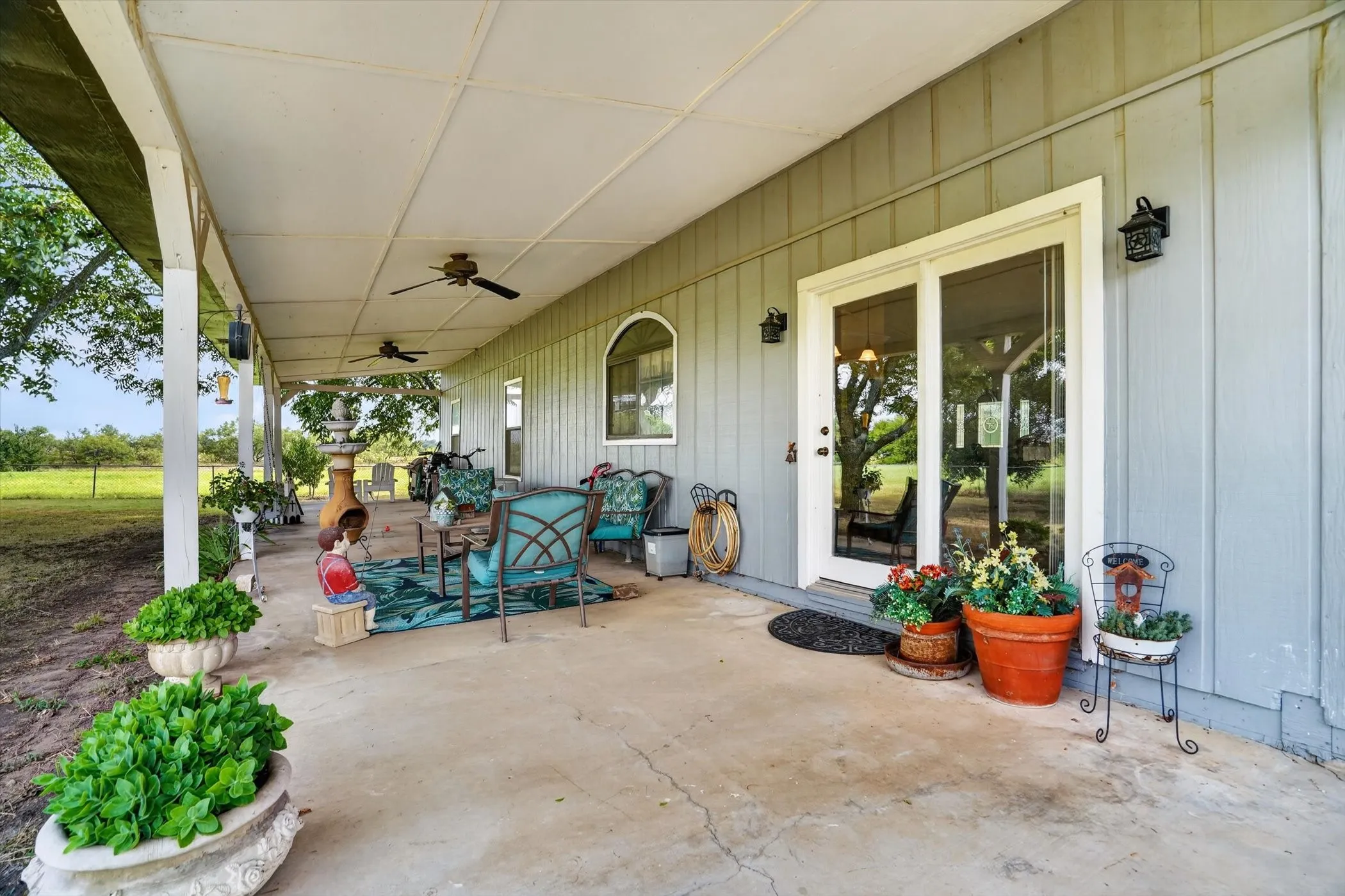 Expansive covered concrete patio featuring ceiling fans, sliding glass door access, exterior wall sconces, and an arched window