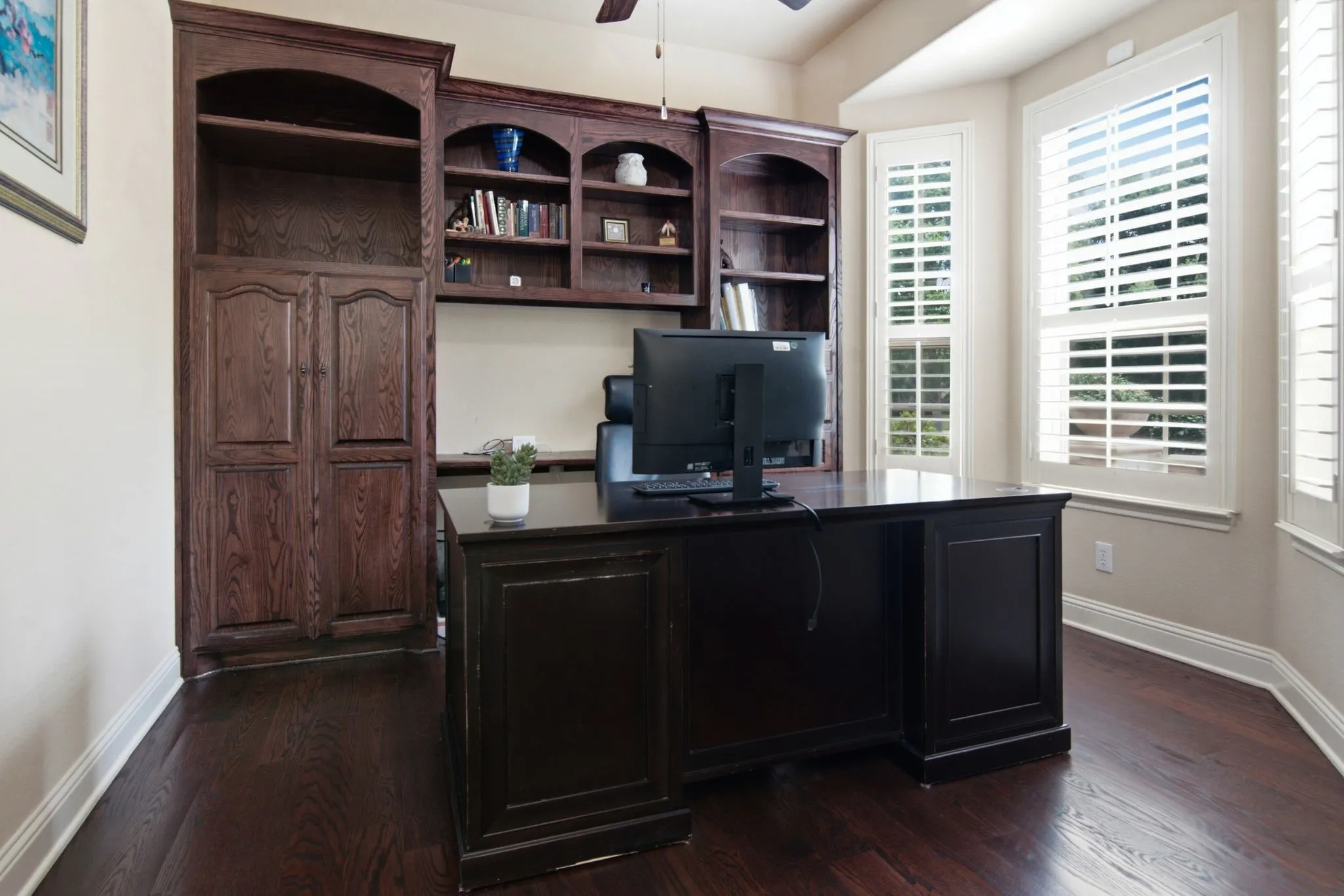 Executive study with built in bookcase, bay window, plantation shutters, and french dooors.