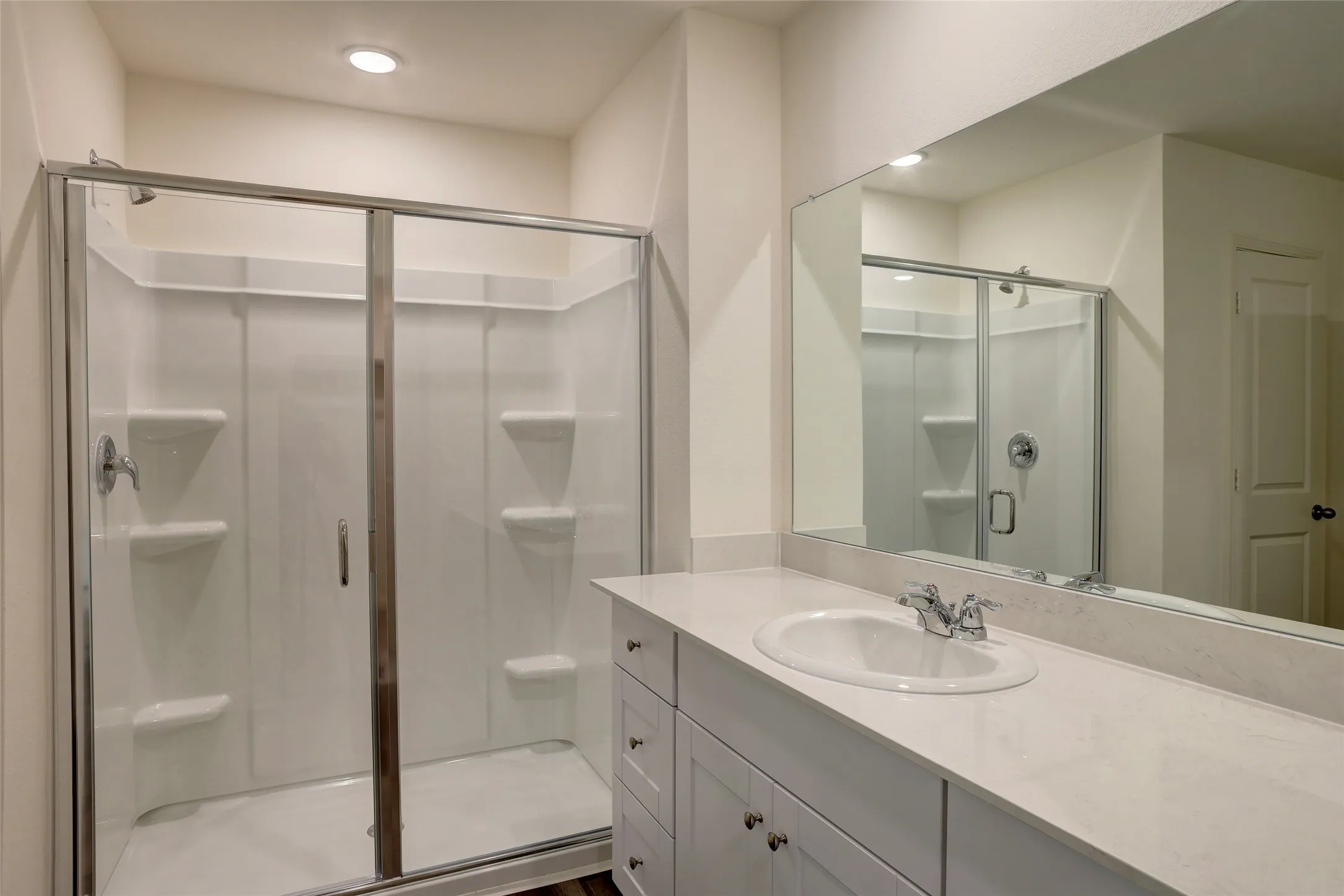 Bathroom featuring a glass-enclosed shower with integrated shelving, a single vanity with an undermount sink, and a large wall-mounted mirror