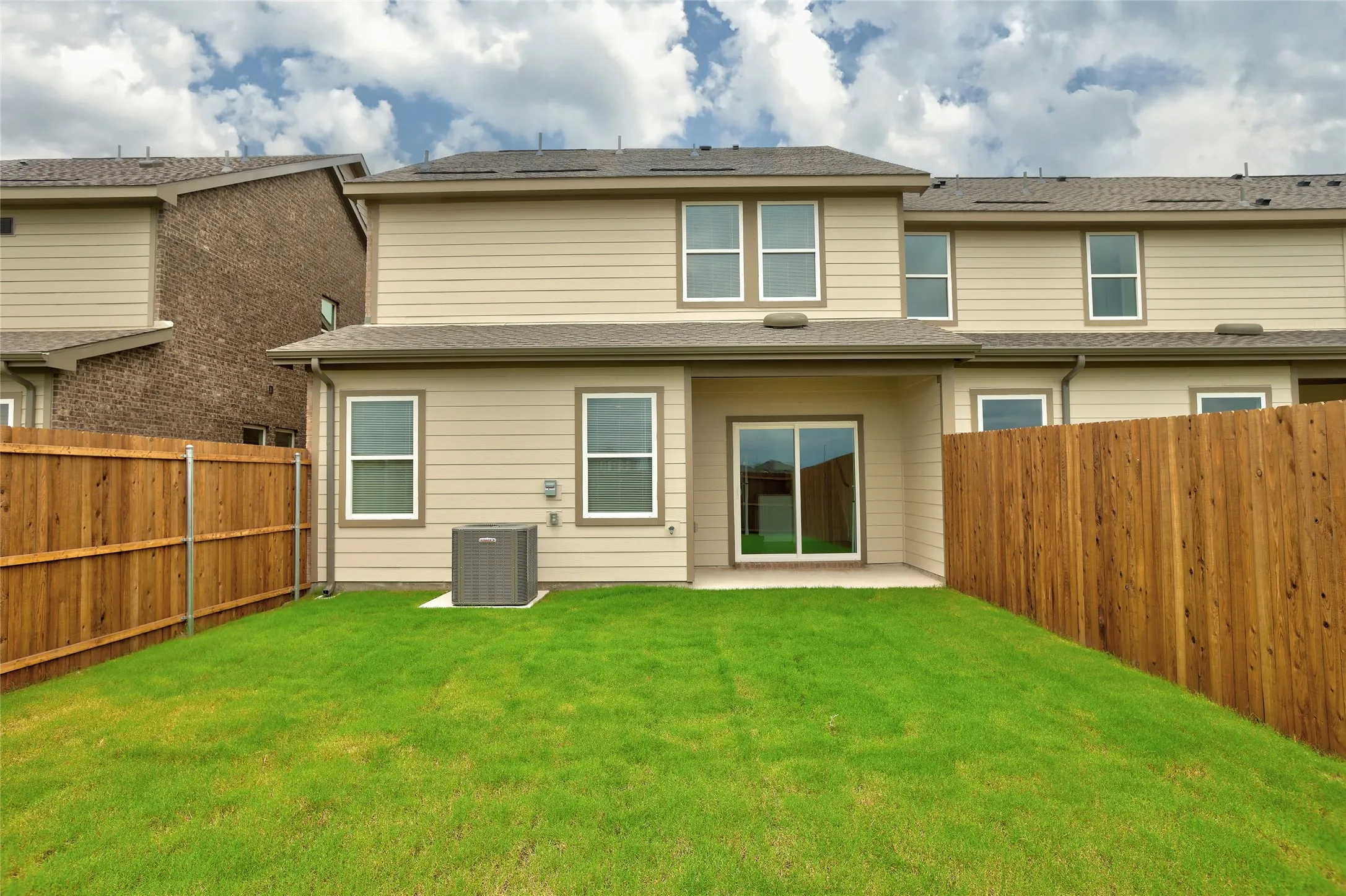 Private fenced backyard featuring a grassy lawn, concrete patio, and sliding glass door access to the interior