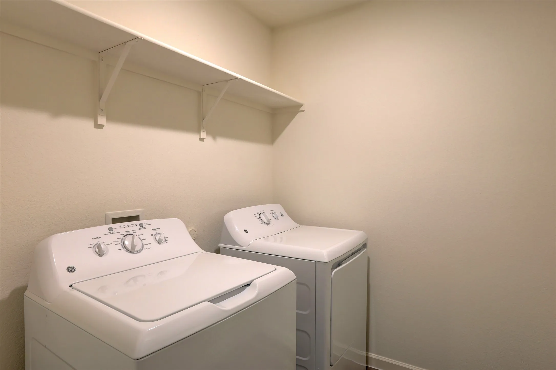 Dedicated laundry area featuring a white top-loading washing machine, a white front-loading dryer, and a wall-mounted white storage shelf