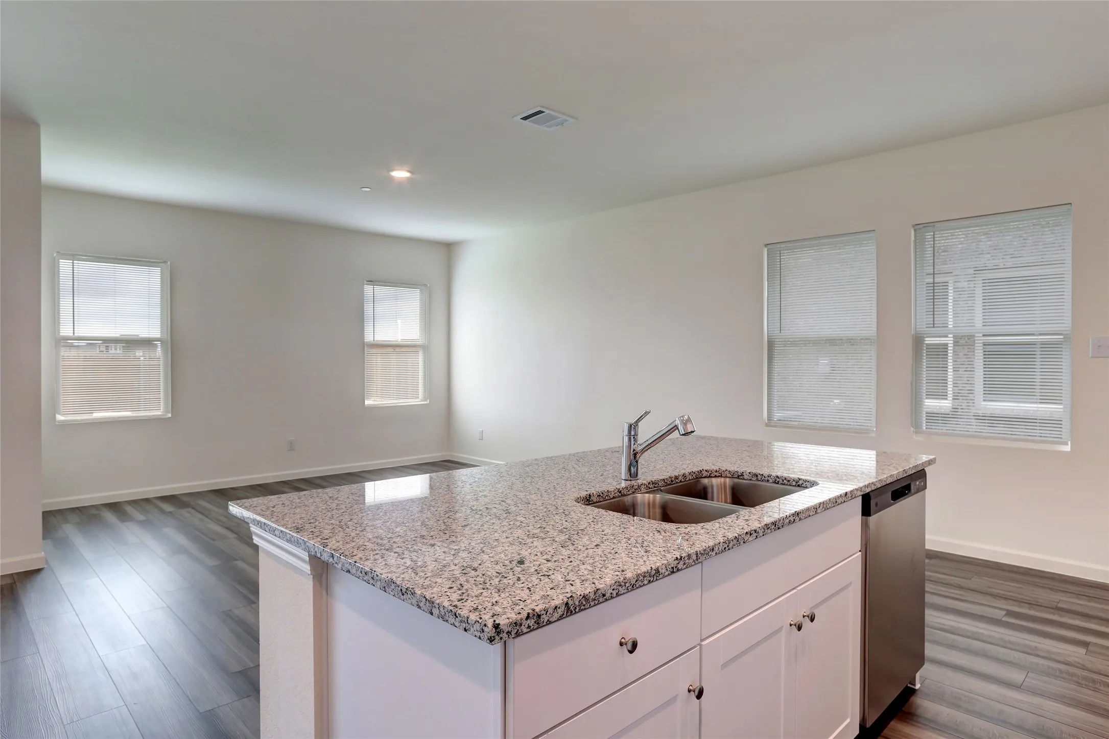 Kitchen island with a light-toned speckled countertop, integrated stainless steel double basin sink, and a chrome faucet