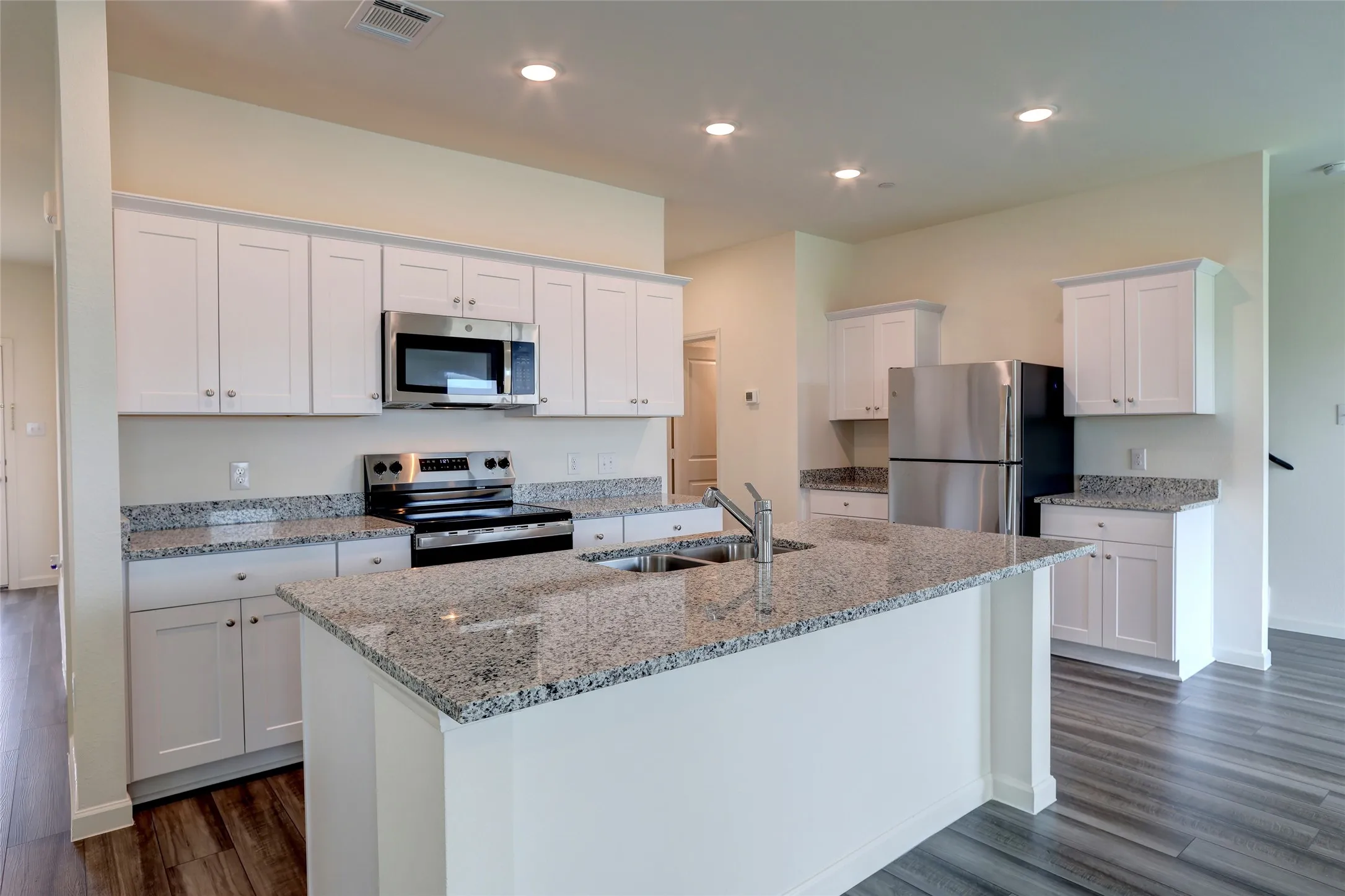 Modern kitchen featuring a central island with an undermount sink, light granite countertops, white cabinetry, stainless steel appliances, and wood-finish flooring