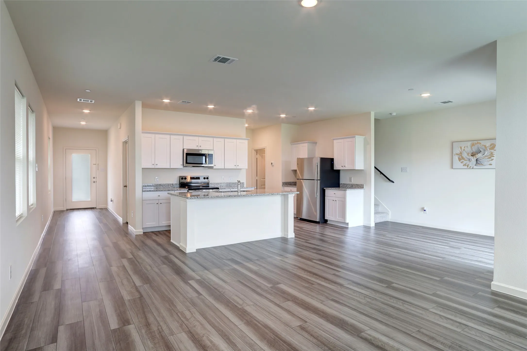 Open-concept living space featuring wood-finish flooring, recessed lighting, and a kitchen island with stone countertops