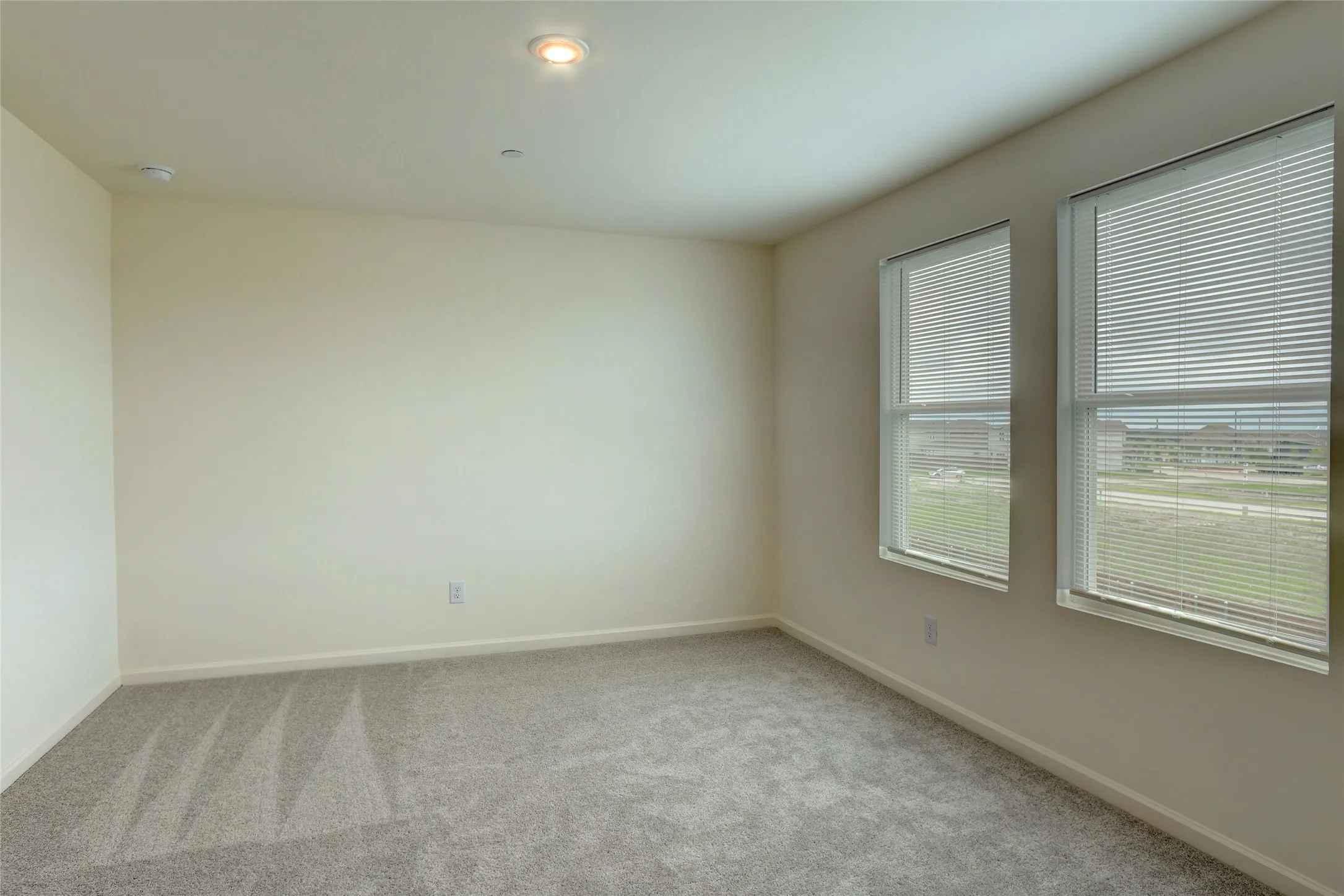 Bright room featuring two large windows with blinds, neutral-toned walls, and grey carpeting