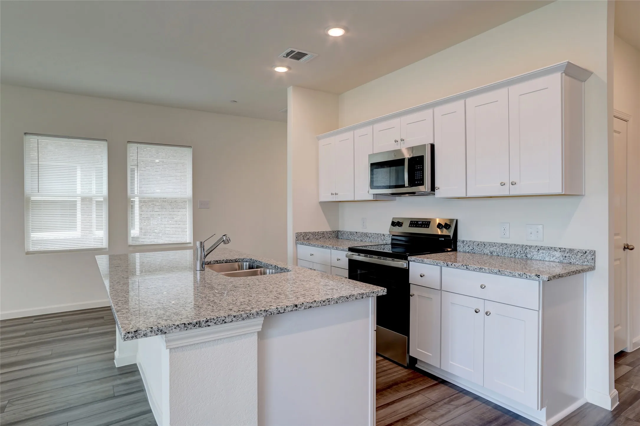 Modern kitchen featuring white shaker cabinetry, stainless steel appliances, speckled stone countertops, a kitchen island with an undermount sink, and wood-finish flooring