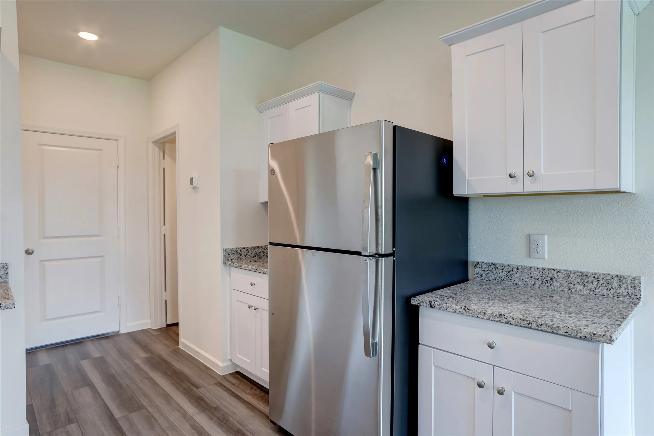 Kitchen area featuring stainless steel refrigerator, white cabinetry with silver hardware, speckled countertops, and wood-finish flooring