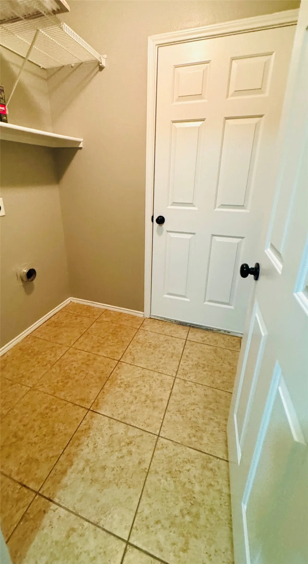 Utility space featuring light beige walls, tiled flooring, white panel doors with black hardware, and a white wire shelving unit