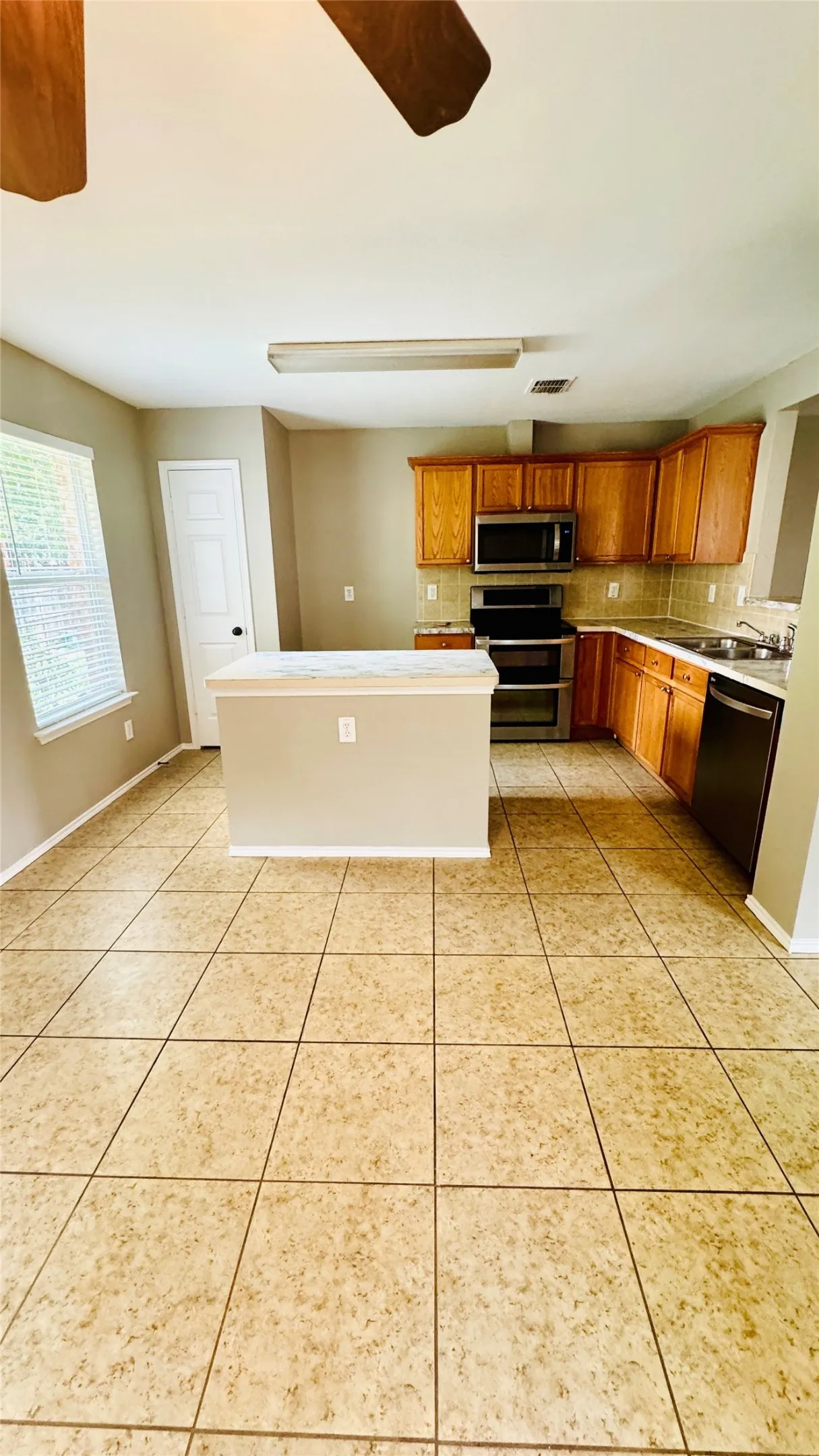 Kitchen featuring a central island with a light-toned countertop, wood-finish cabinetry, stainless steel appliances, and tile flooring