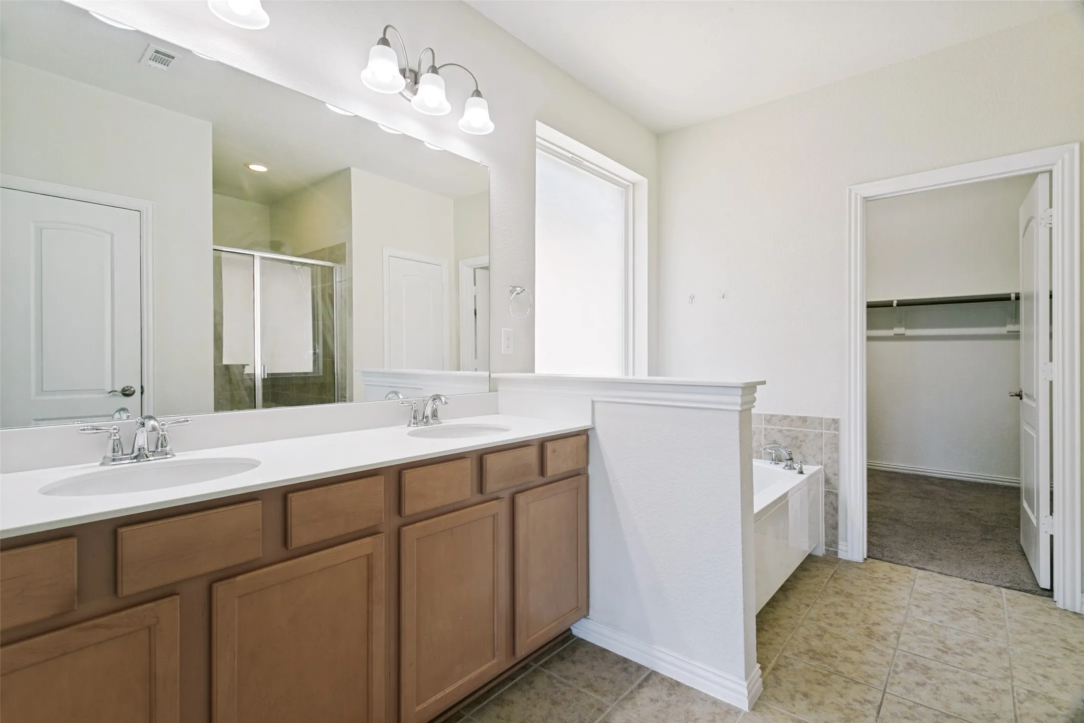 Bathroom featuring a dual vanity with white countertops, light wood-finish cabinetry, and chrome fixtures