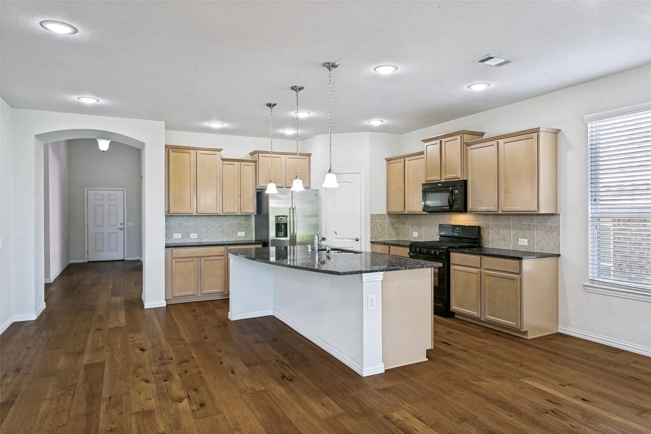 Kitchen featuring a large island with dark countertops, wood-finish flooring, light cabinetry, and recessed lighting