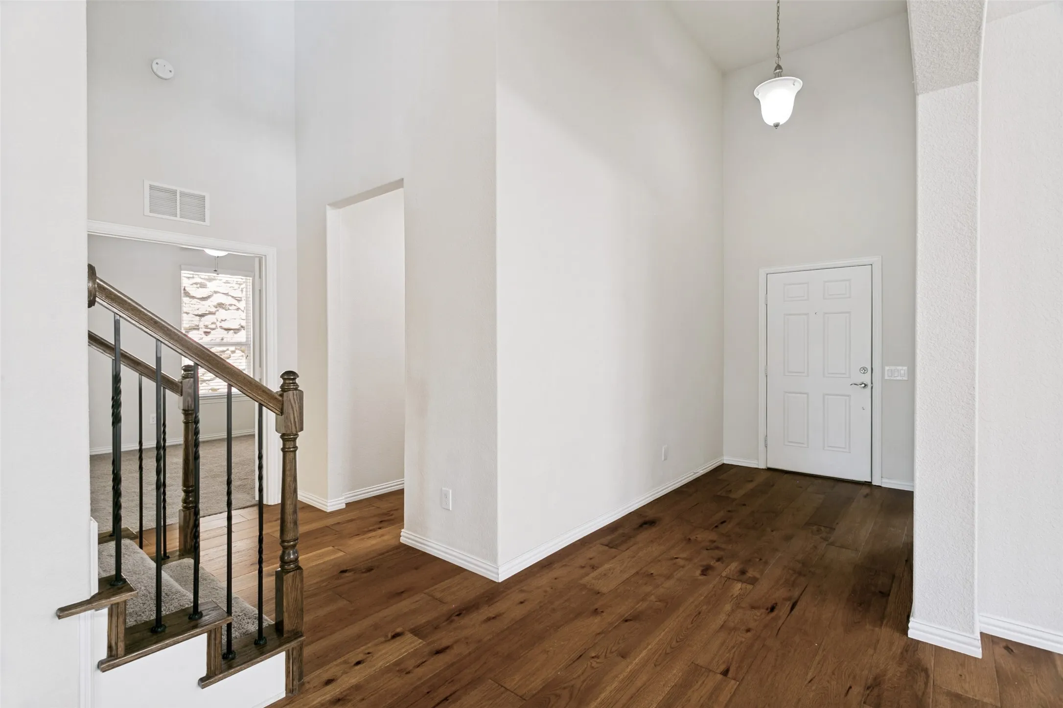 Entryway featuring wood-finish flooring, high ceilings, a white paneled door, and a traditional pendant light fixture