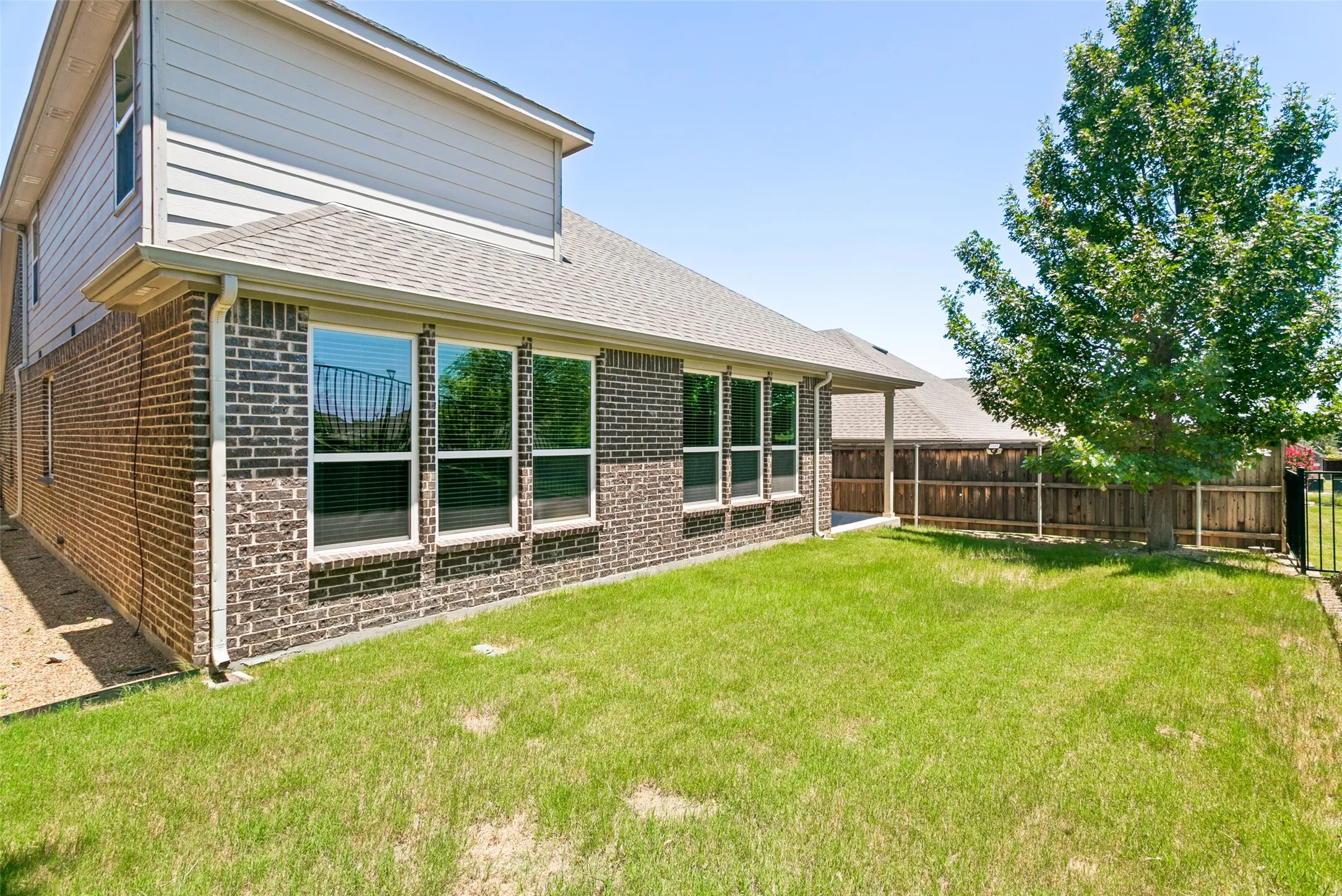 Expansive lawn area featuring a mature tree, privacy fencing, and a partial black metal fence
