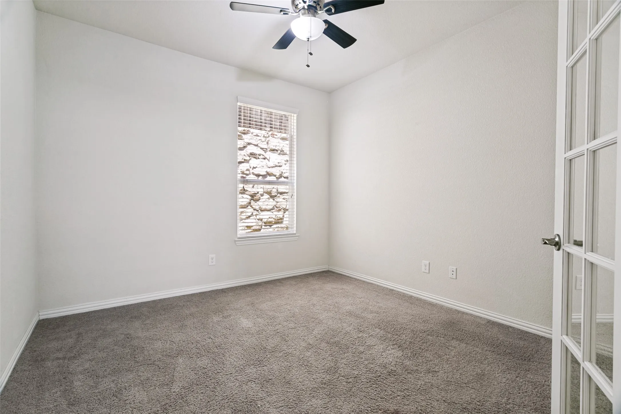 Carpeted room featuring a ceiling fan with light kit, a window with horizontal blinds, and a white French door