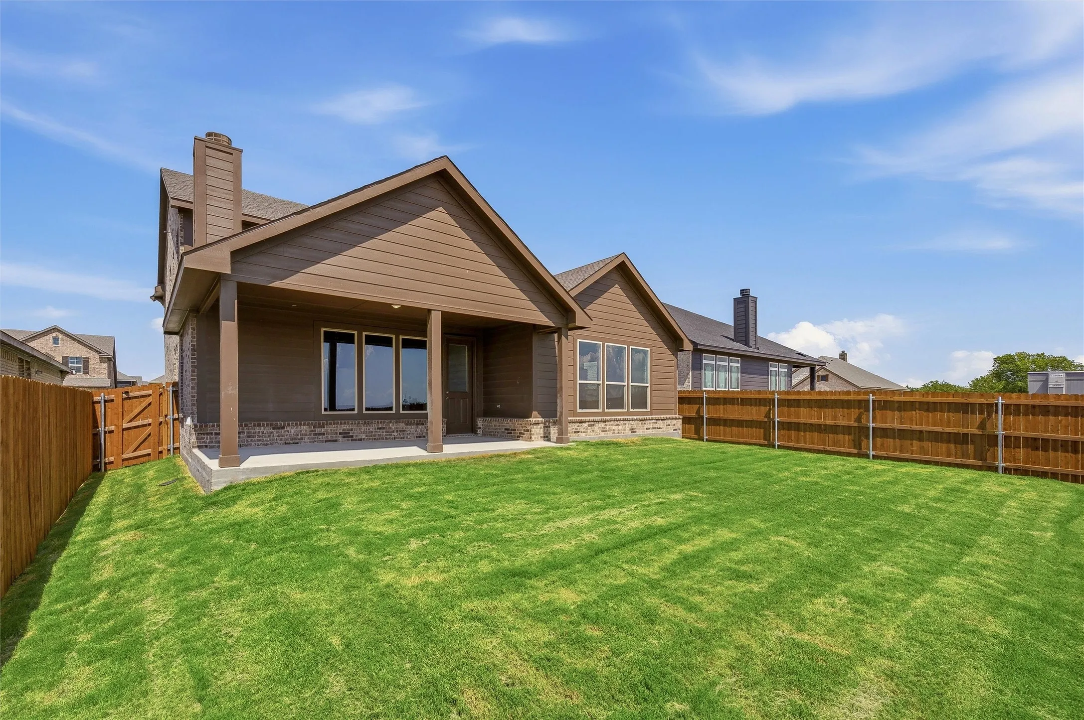 Expansive backyard featuring a manicured lawn, full privacy fencing, and a covered patio