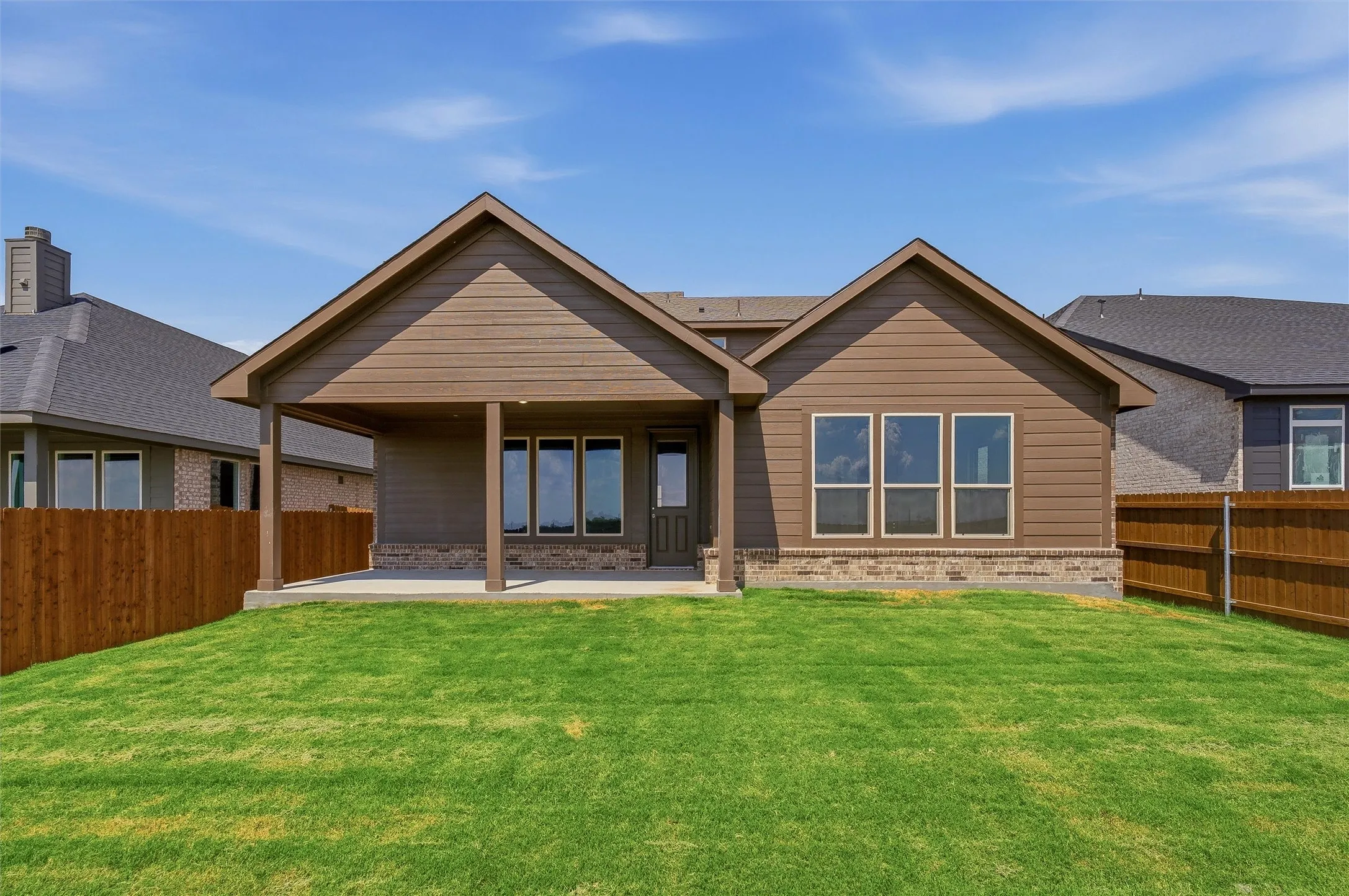 Expansive backyard featuring a concrete patio, covered porch with columns, and a full wood fence