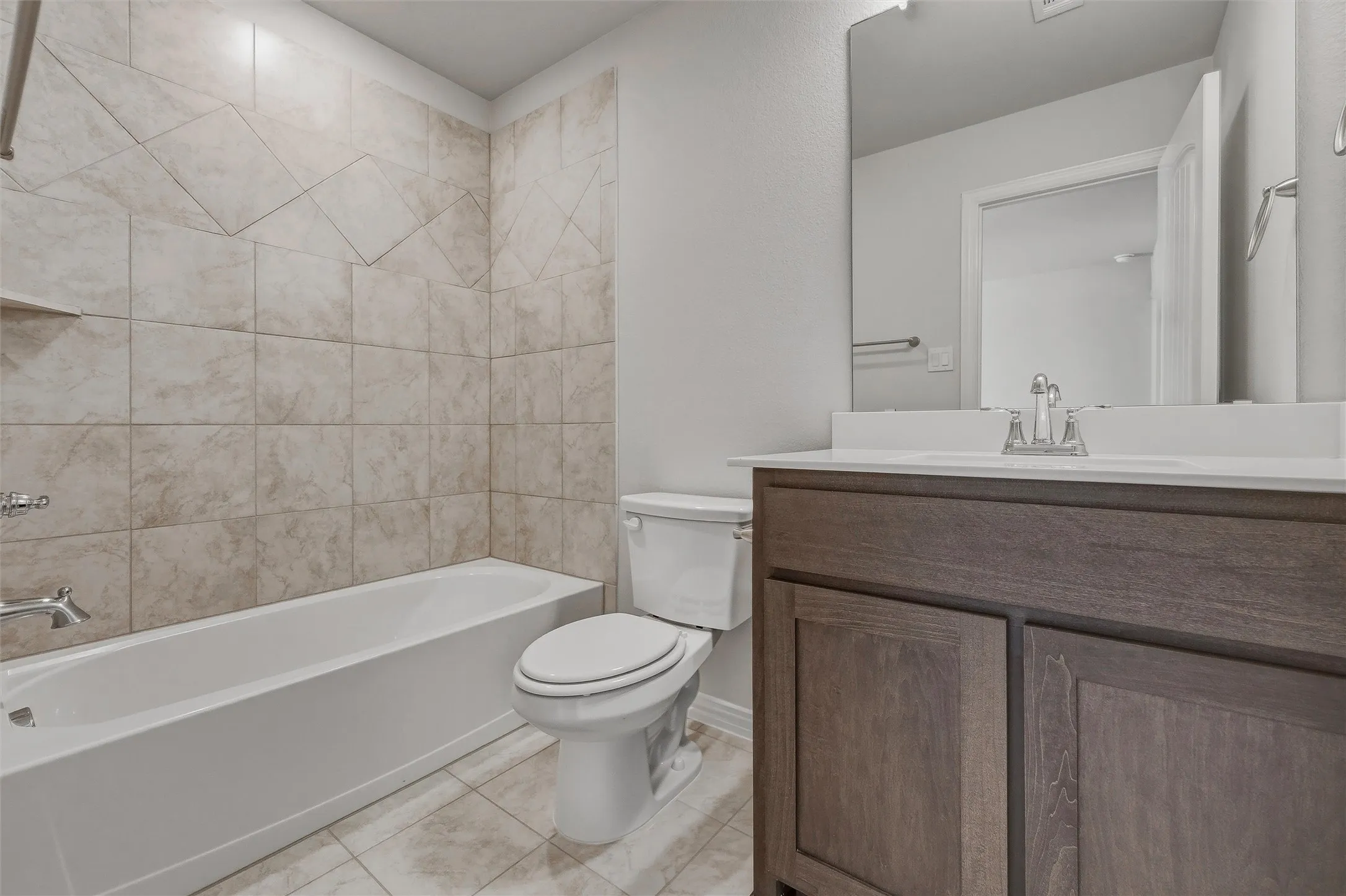 Bathroom featuring a built-in bathtub with tiled surround, a toilet, a vanity with a white countertop, and a wall-mounted mirror