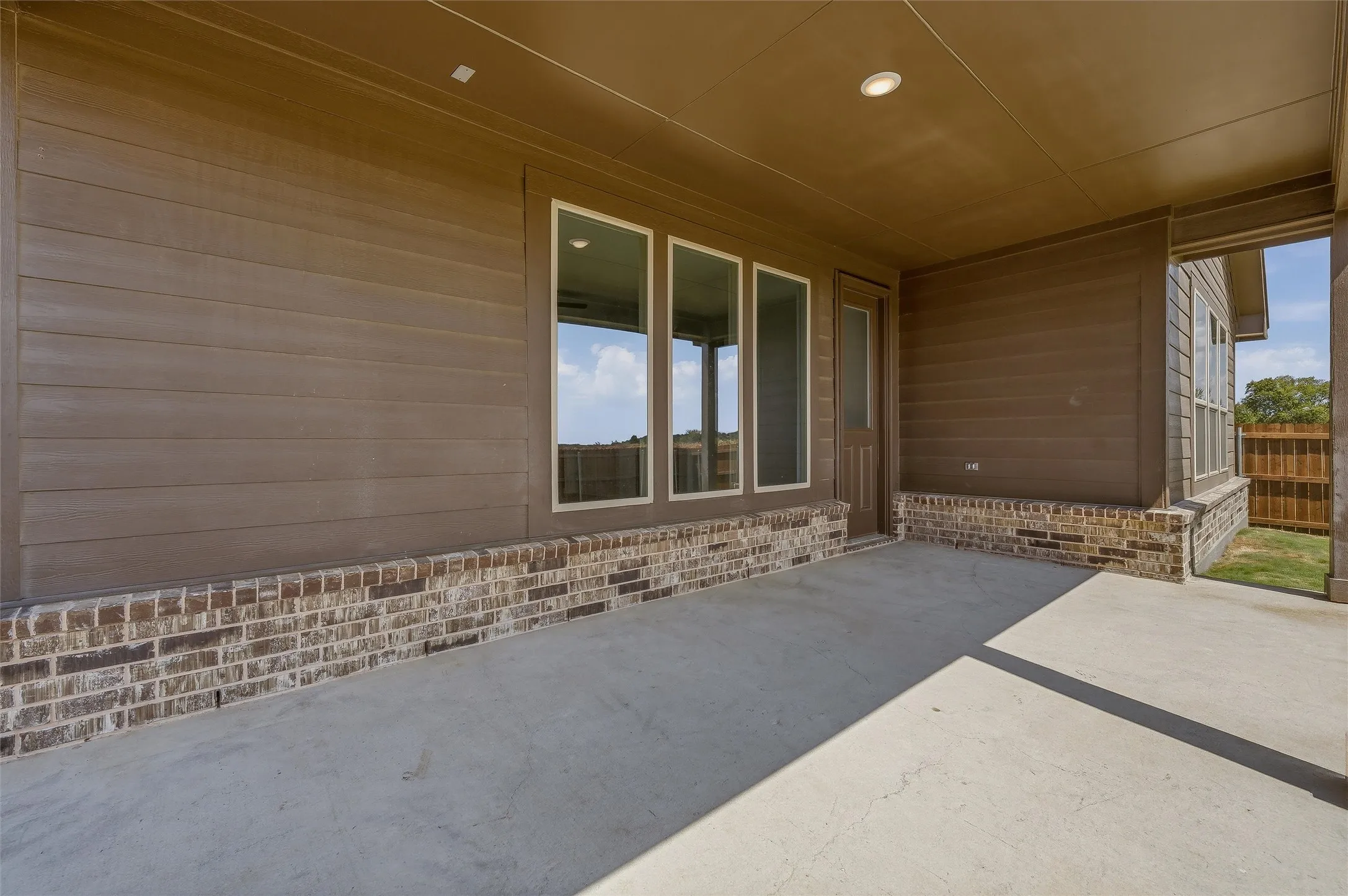 Covered patio with a concrete surface, brick base, horizontal siding, and multiple windows