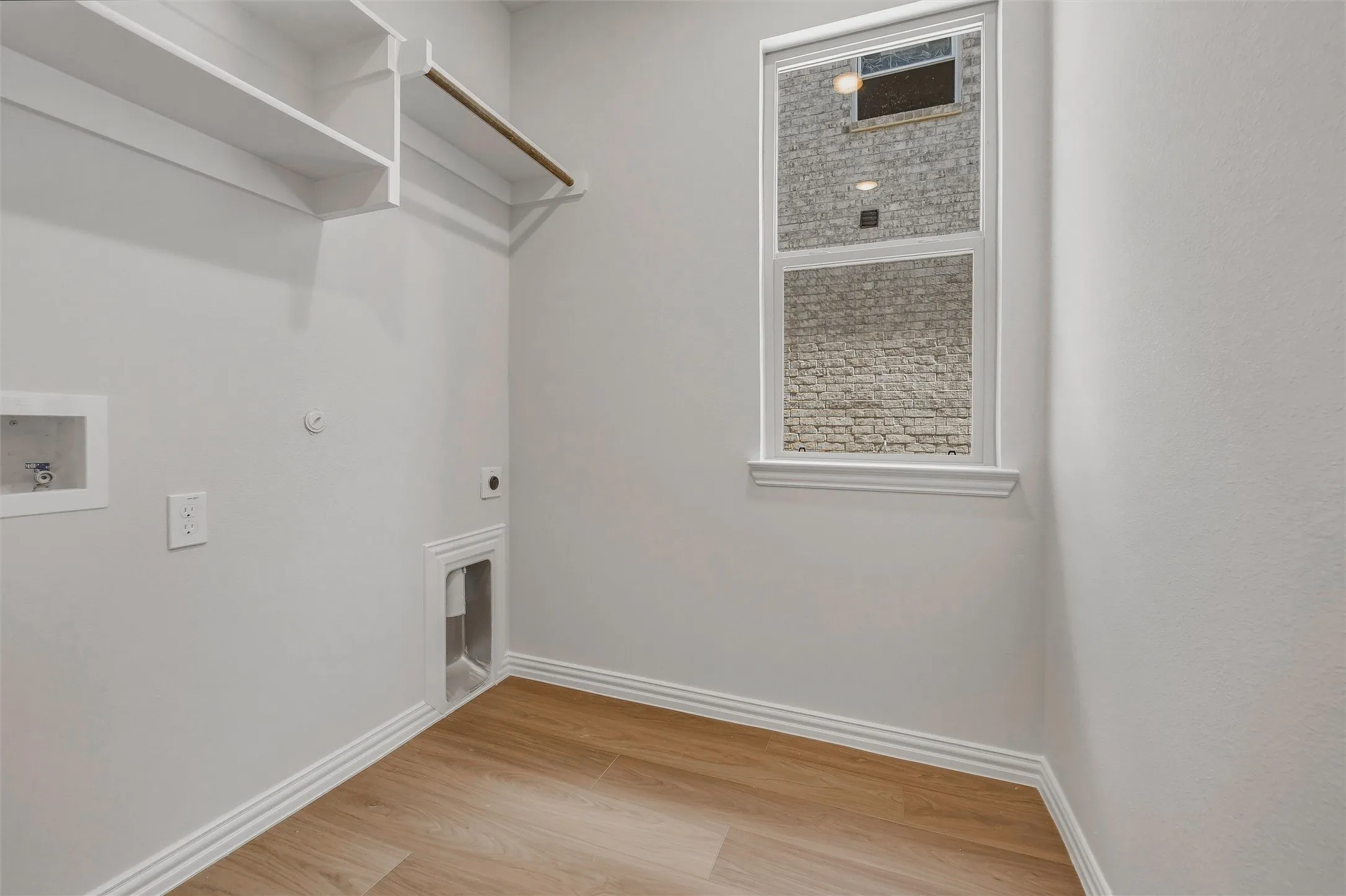 Utility room featuring wood-finish flooring, a double-paned window, and built-in shelving with a clothes rod