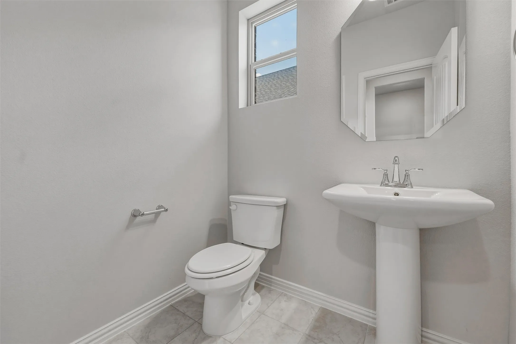 Pedestal sink with chrome faucet, toilet, and window providing natural light