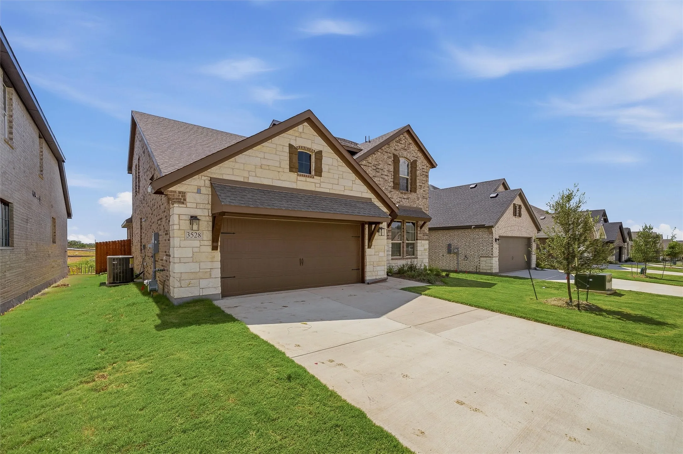 Stone and brick facade, two-car garage, concrete driveway, architectural shingle roof, decorative window shutters