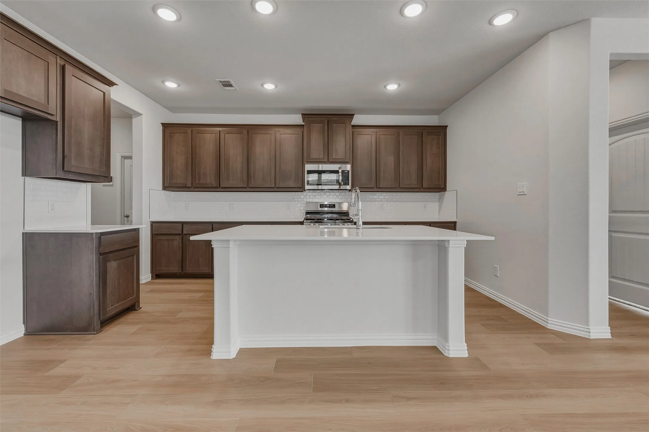 Kitchen featuring wood-finish flooring, recessed lighting, a central island with a white countertop, and dark wood cabinetry