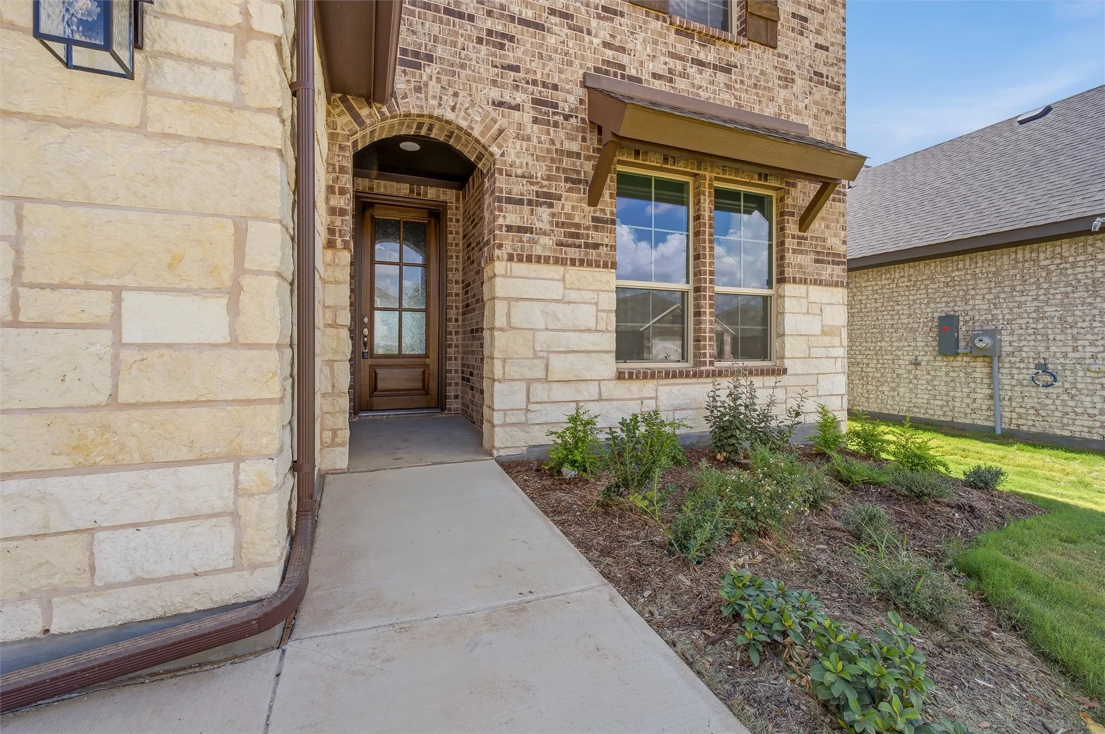 Brick and stone exterior featuring an arched entryway and a wood-panel front door with glass inserts