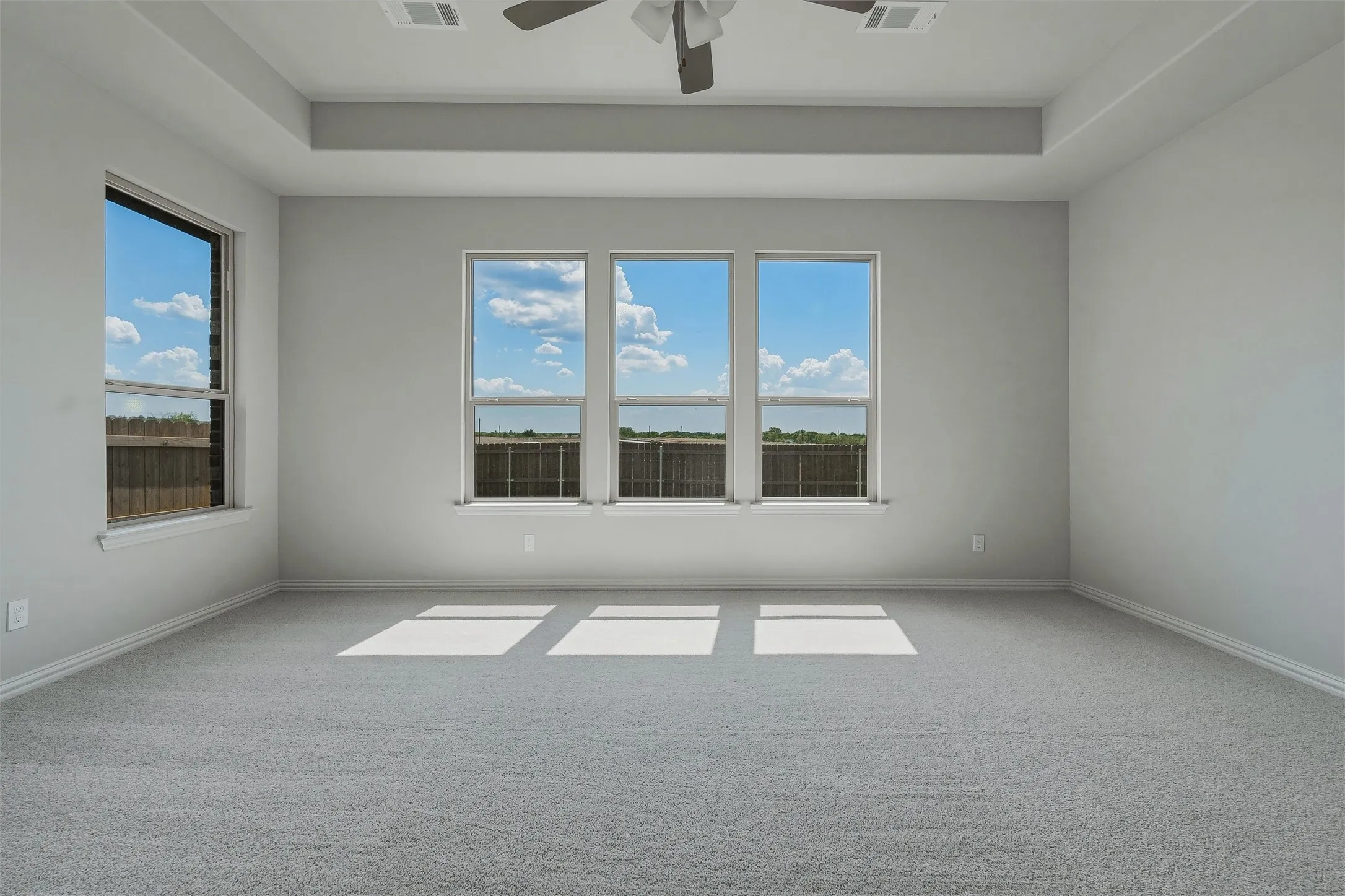 Tray ceiling with recessed lighting, ceiling fan, grey carpet flooring, and multiple windows