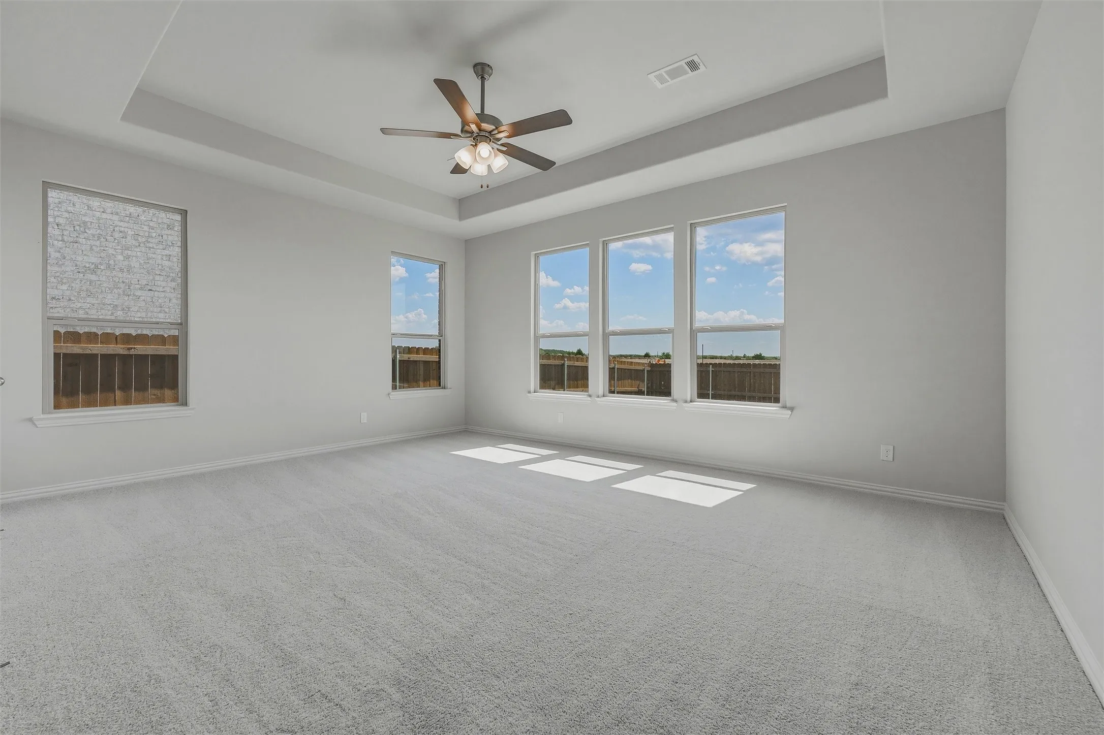 Spacious room featuring light gray carpeting, a tray ceiling, and a ceiling fan with integrated lighting