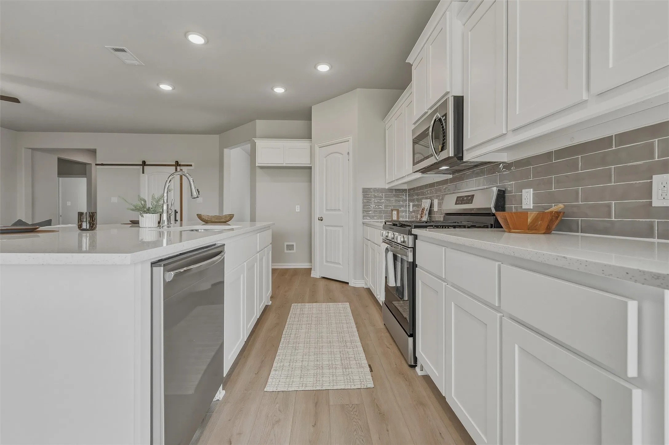 Kitchen featuring white shaker-style cabinetry, stainless steel appliances, a subway tile backsplash, recessed lighting, and wood-finish flooring