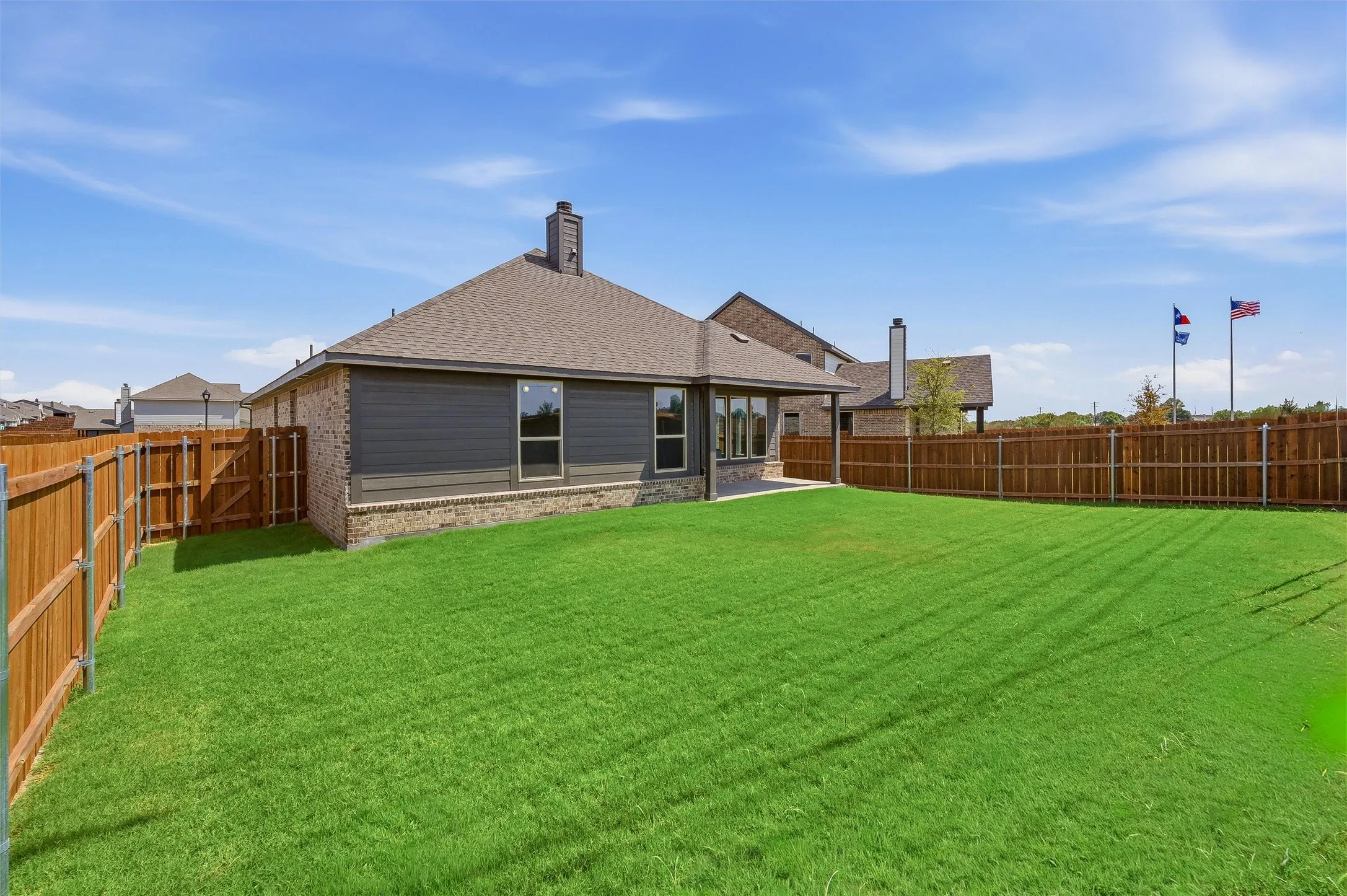Expansive fenced backyard with a manicured lawn, brick and siding exterior, and a covered patio