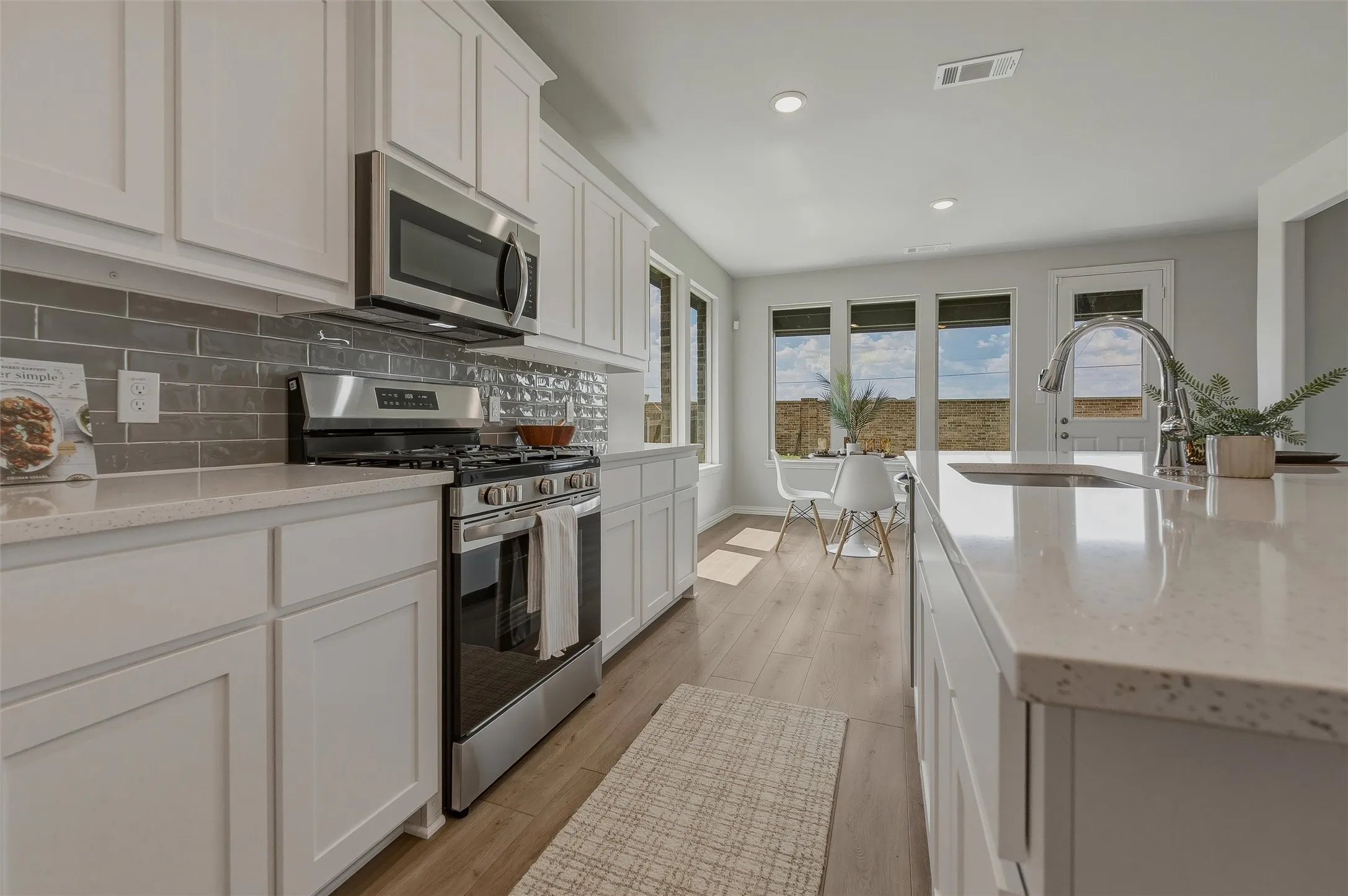 White shaker-style cabinetry, stainless steel appliances, light-toned countertops, and wood-finish flooring